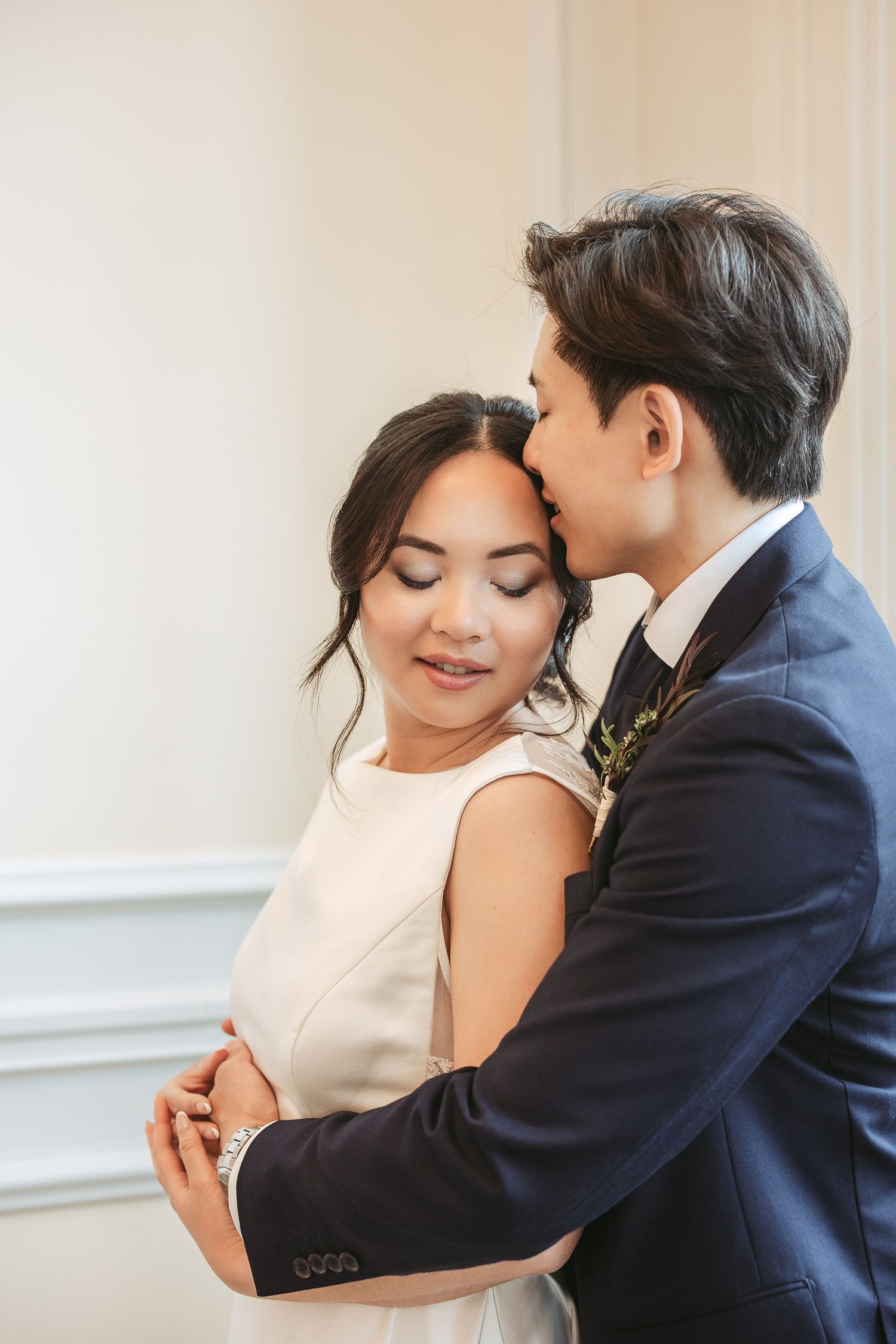 Couple de mariés s’enlaçant lors d’une séance photo de mariage, la mariée en robe blanche et le marié en costume bleu marine