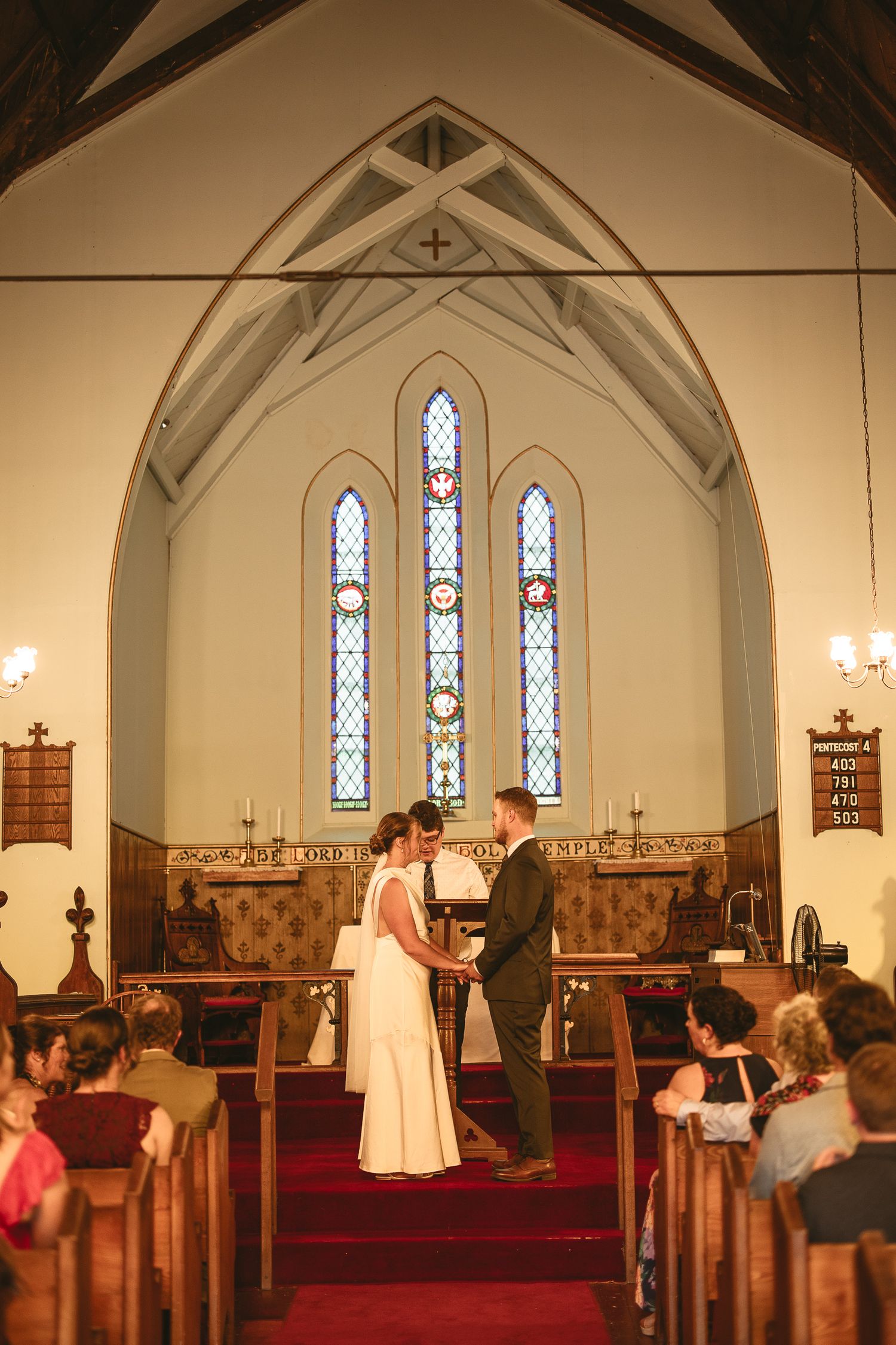 Cérémonie de mariage dans une église traditionnelle aux vitraux colorés et bancs en bois, remplie d’invités