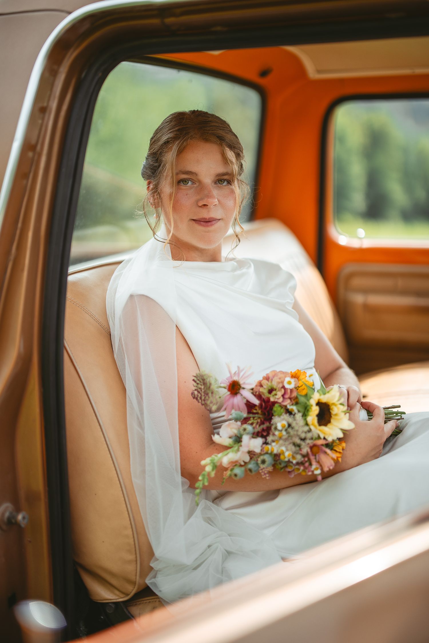 Mariée dans une voiture vintage à intérieur beige tenant un bouquet de tournesols