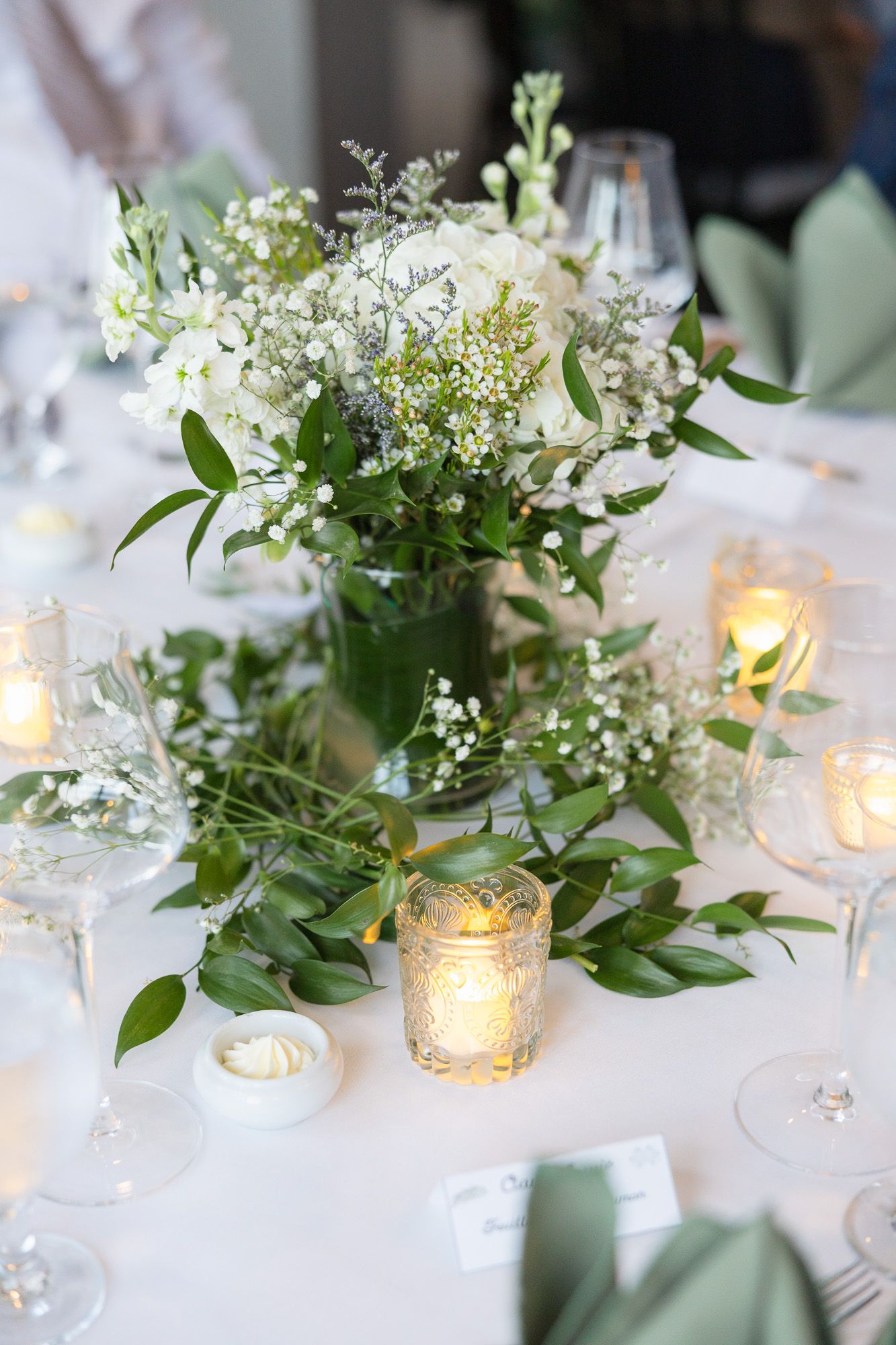 Mise en place de table élégante avec centres de table floraux blancs, verdure et bougies votives lumineuses