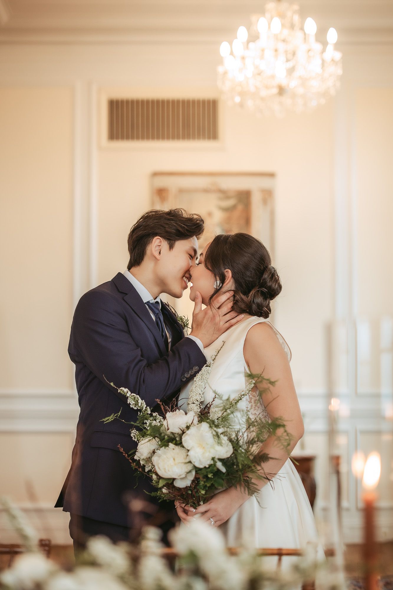 Moment romantique de mariage capté dans une salle de bal élégante avec lustres en cristal et compositions florales blanches
