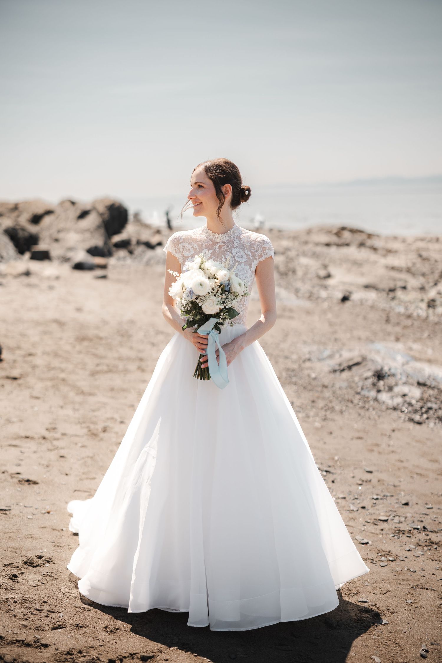 Mariée en robe de mariage blanche classique tenant un bouquet sur le bord du fleuve à l'auberge de la Pointe lors d’une séance photo.