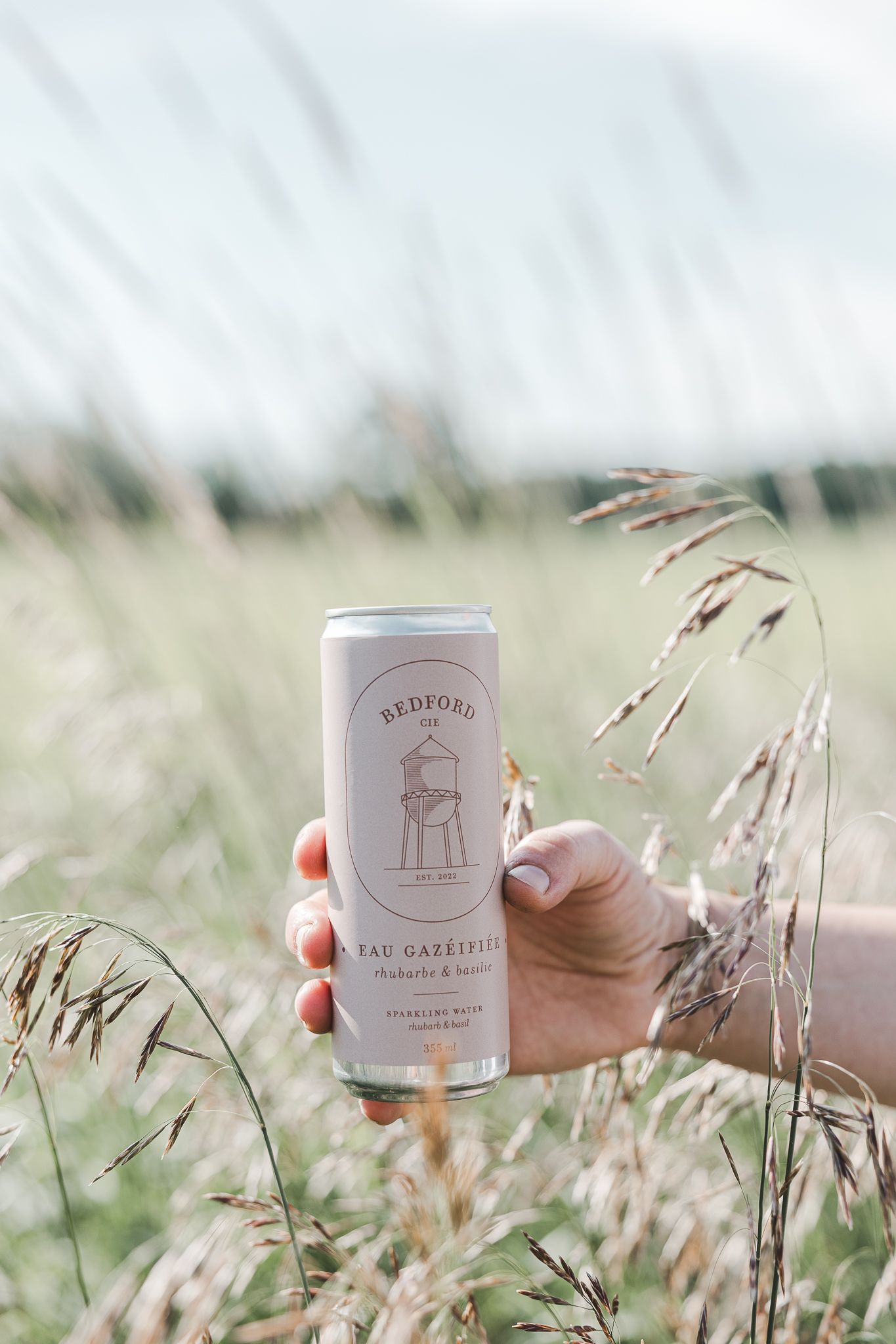 White canned beverages held against a backdrop of tall grass and soft natural lighting.