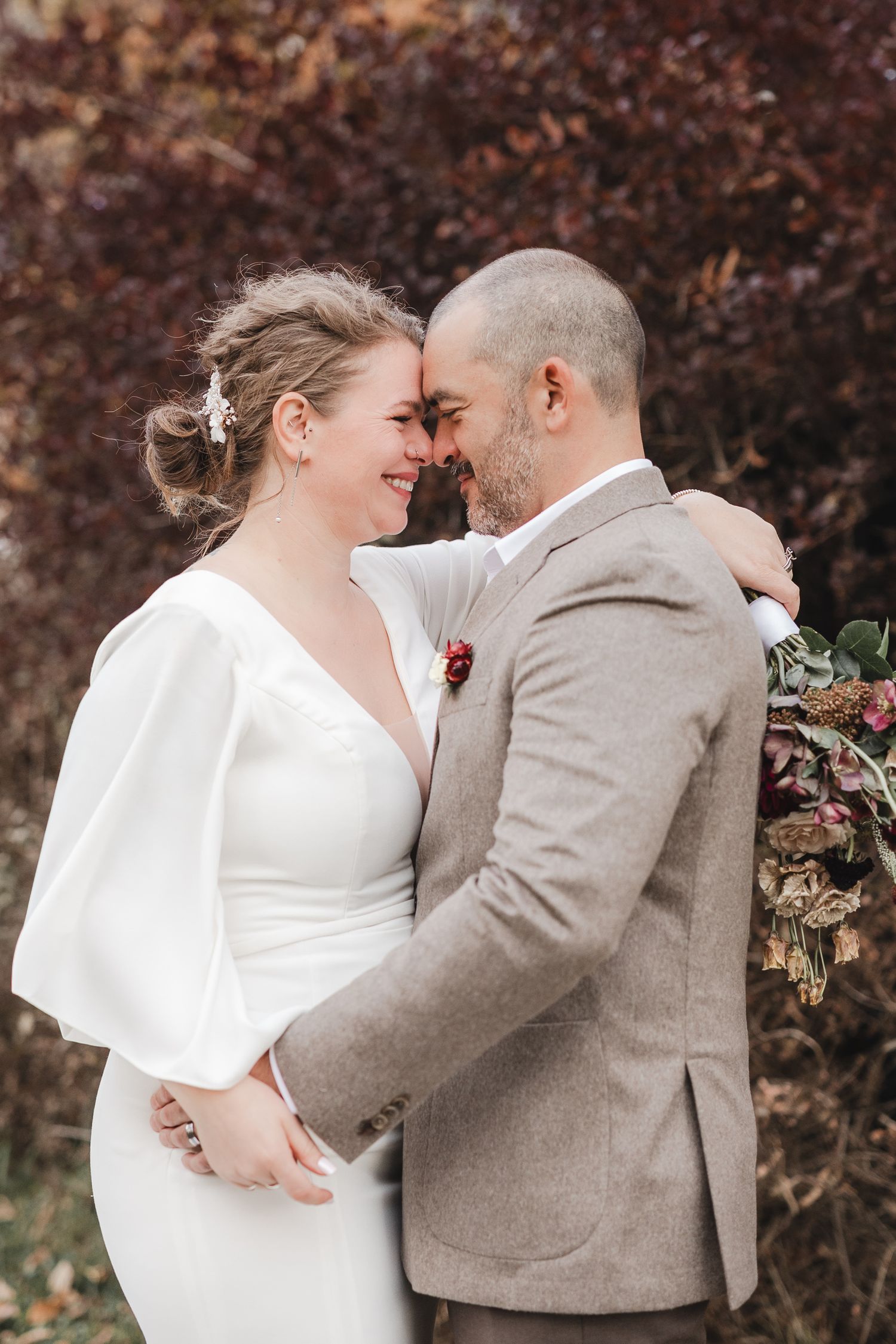 Moment romantique de mariage en extérieur à l’automne, avec feuillage coloré et maisons en arrière-plan.