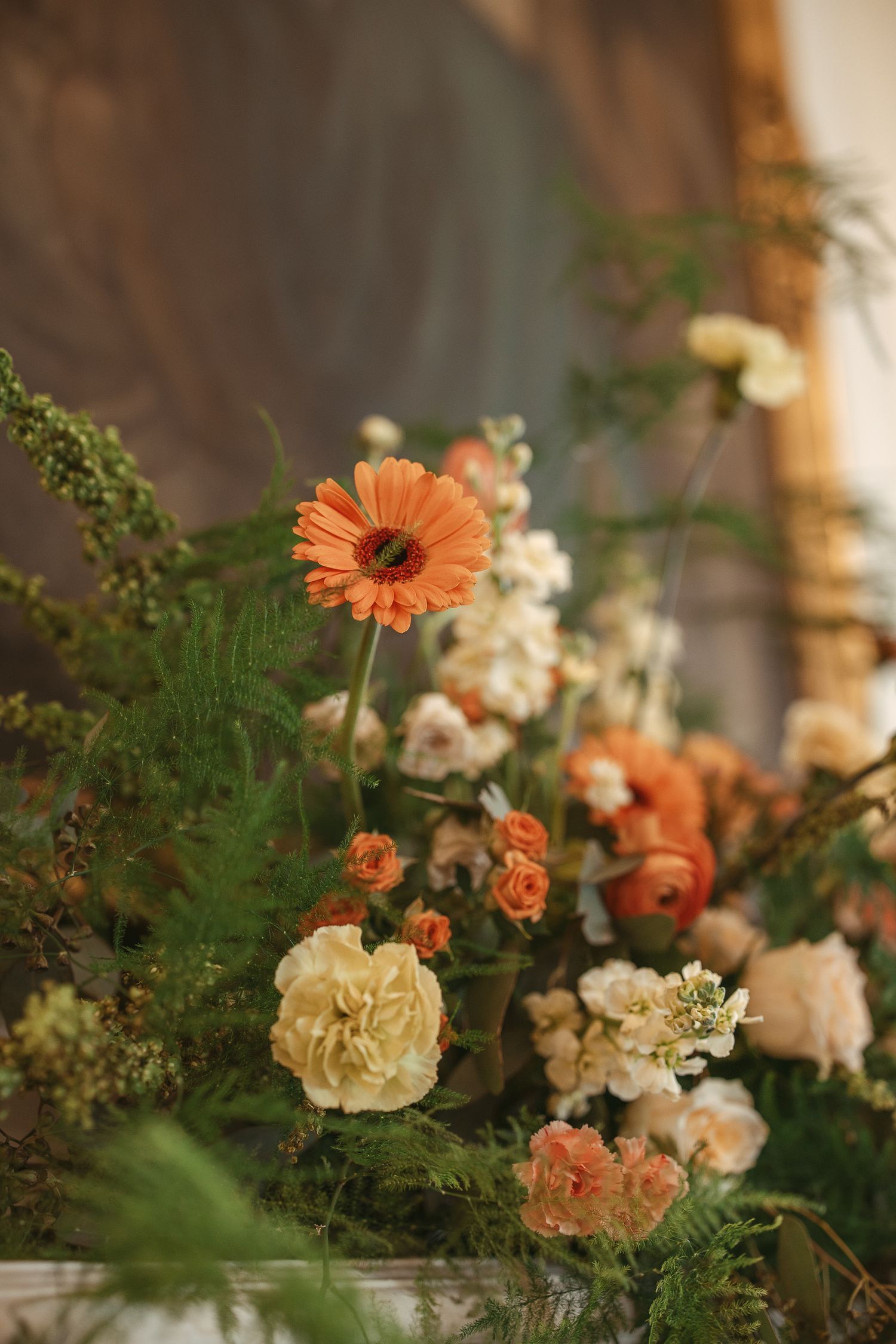 A collection of peach gerbera daisies and cream roses arranged with delicate greenery in a soft, natural light setting.