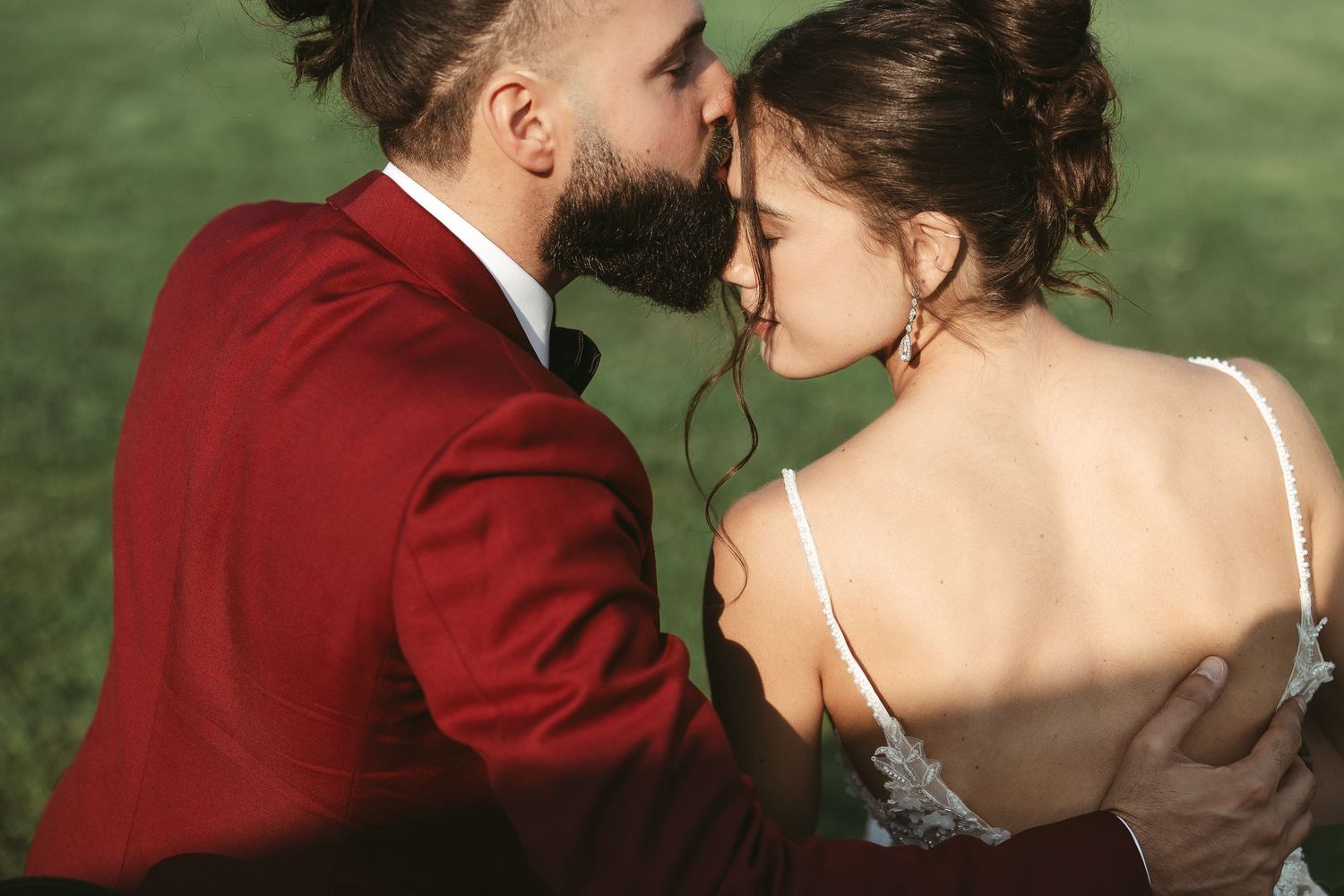 Couple de mariés partageant un moment intime en extérieur, le marié portant un veston bourgogne lors d’un mariage élégant.