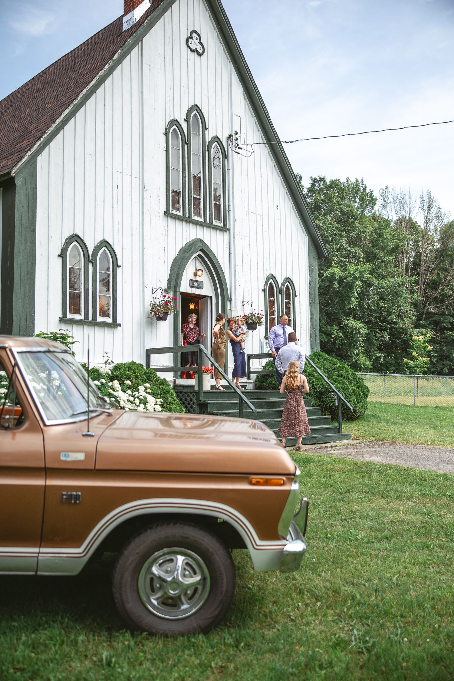 une voiture vintage brune stationnée devant une église blanche sur une pelouse