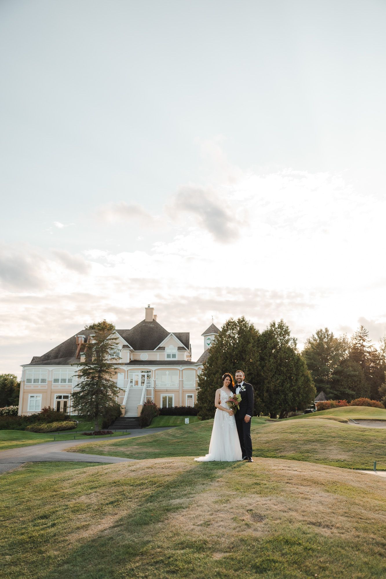 Photos de mariage au coucher du soleil sur une vaste pelouse, avec grande demeure en arrière-plan