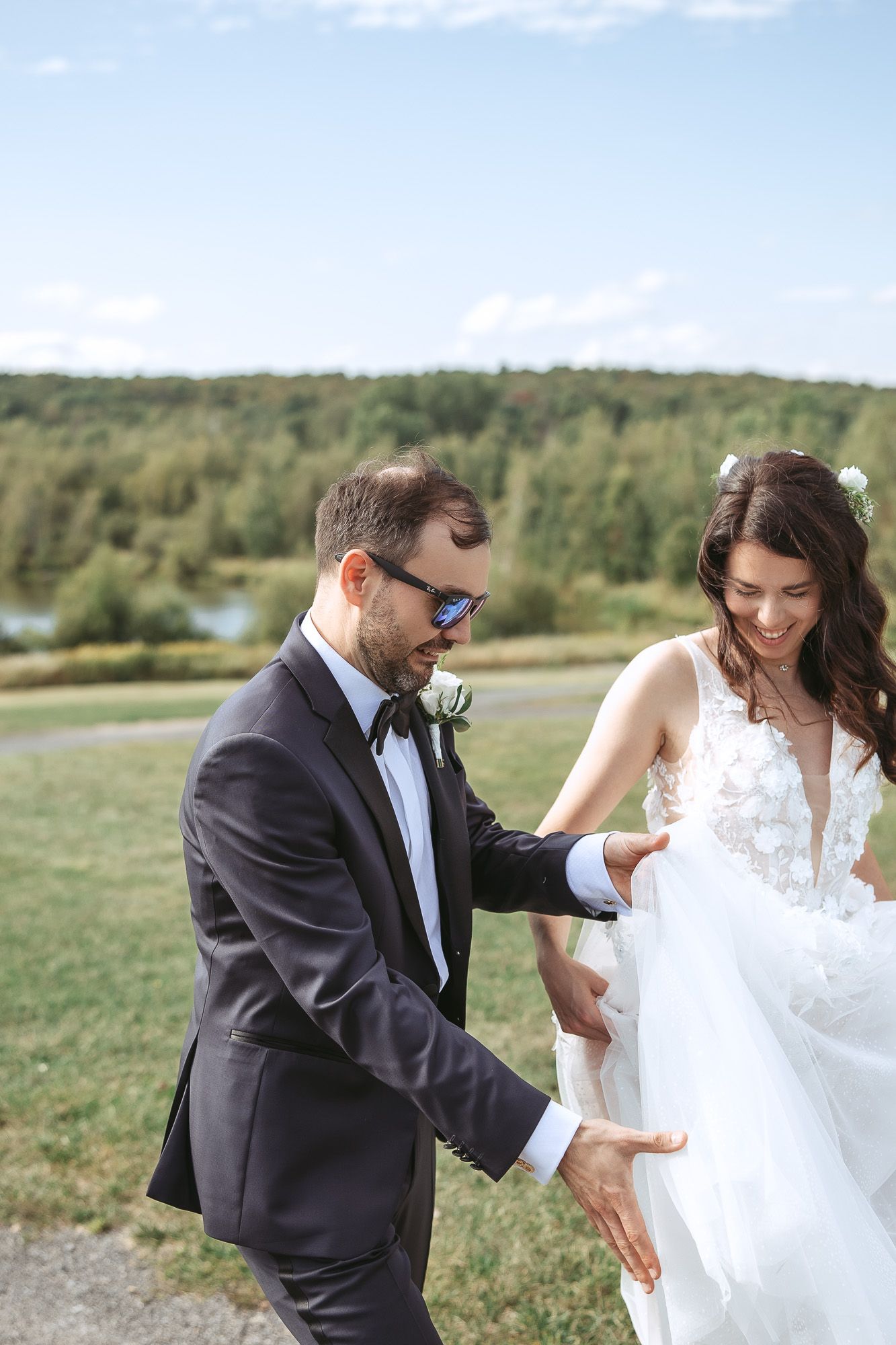 Couple en tenue de mariage partageant un moment ludique en extérieur, dans un champ avec arbres en arrière-plan