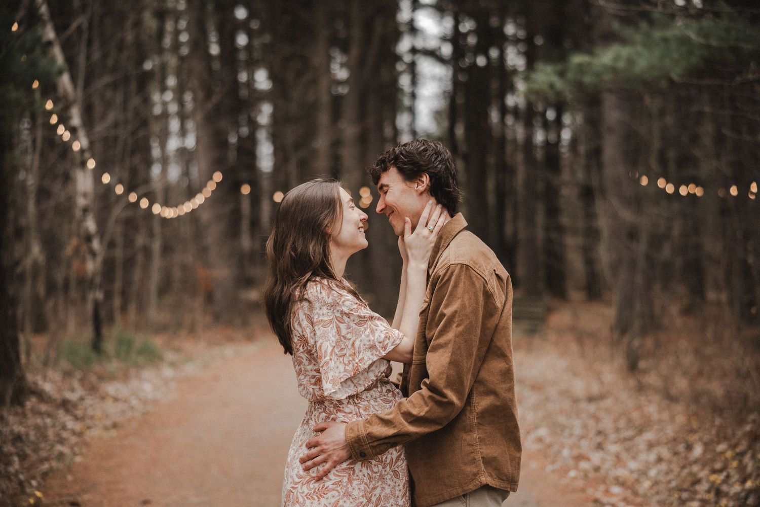 A romantic autumn forest photoshoot with two people embracing among fallen leaves and tall trees.