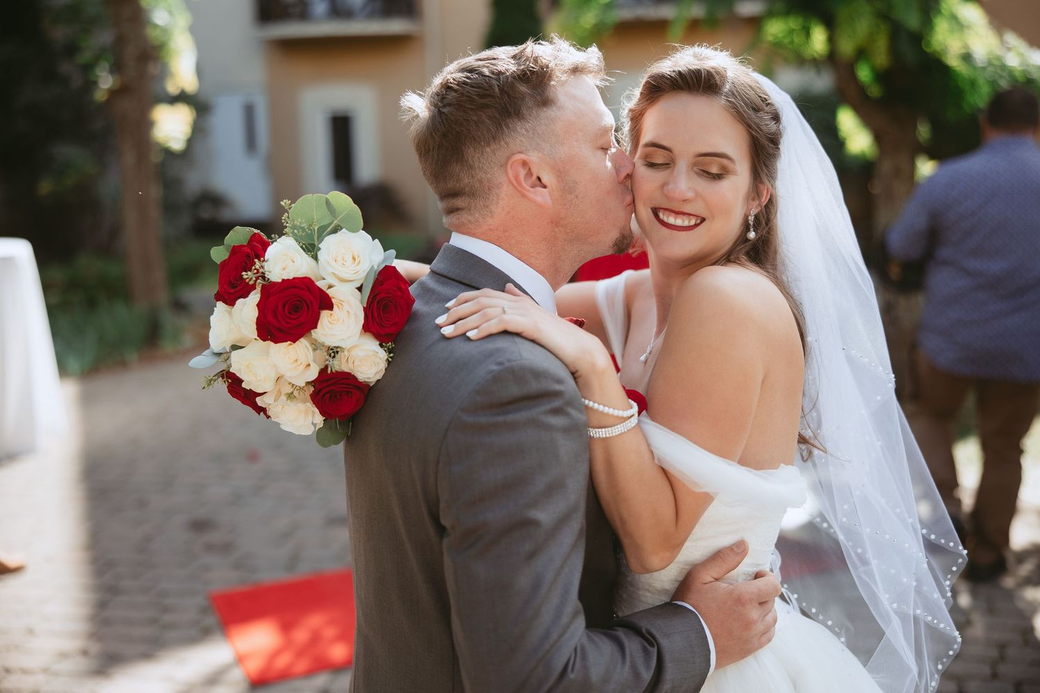 Elegant outdoor wedding ceremony with red rose bouquet and decorative details.