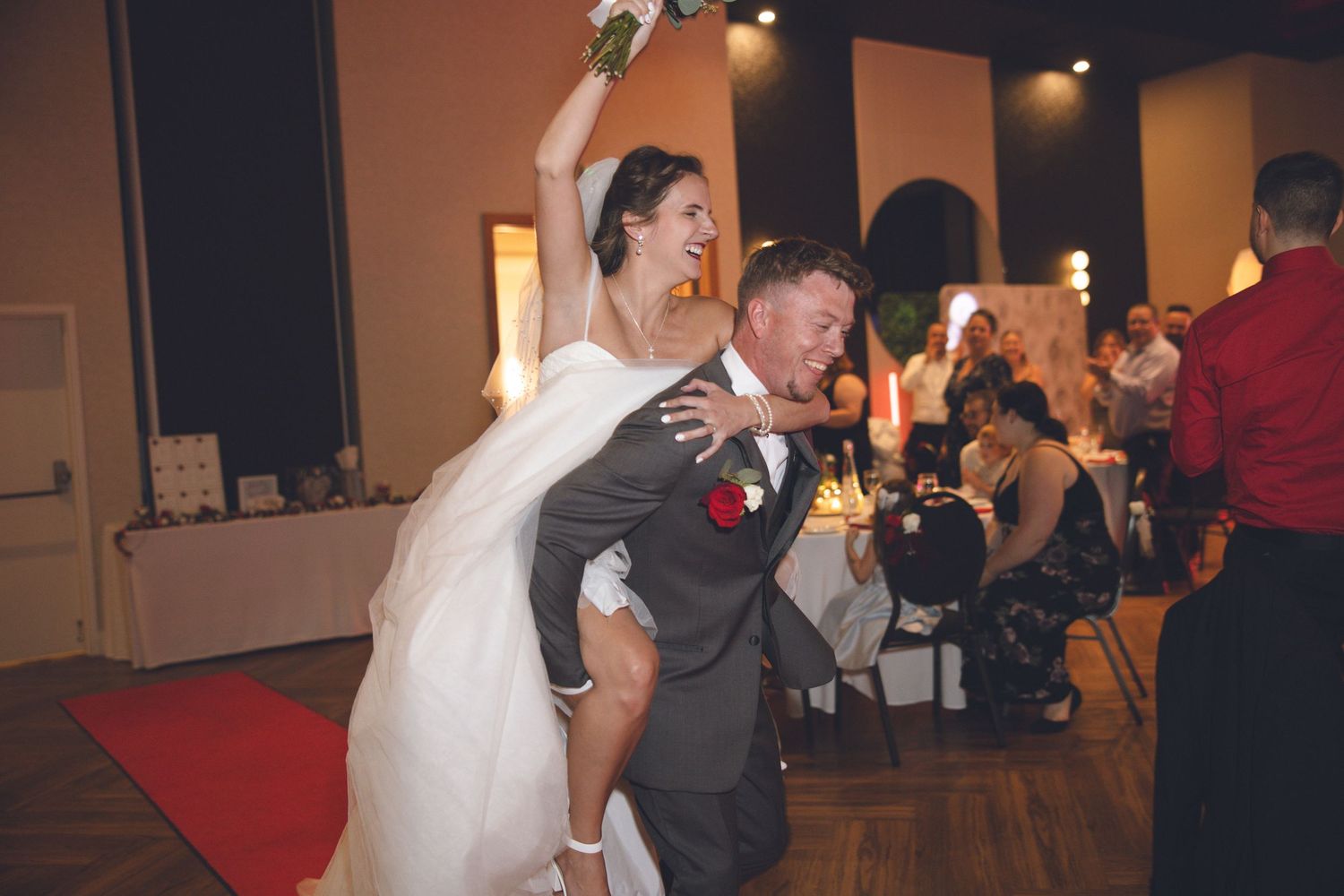 People dancing and celebrating at a wedding reception in a dimly lit venue with warm lighting.