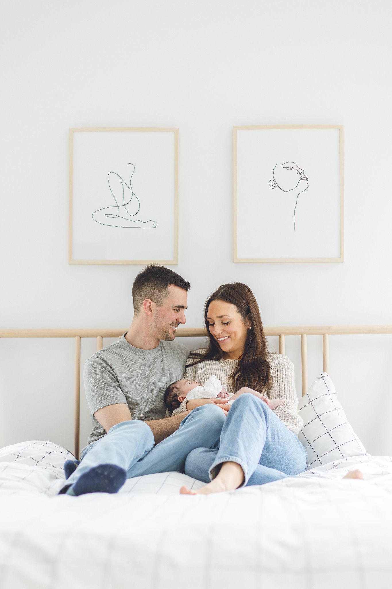 ouple tenant leur nouveau-né sur lit blanc, art mural minimaliste derrière eux, capturé pour moments tendres et intimité familiale