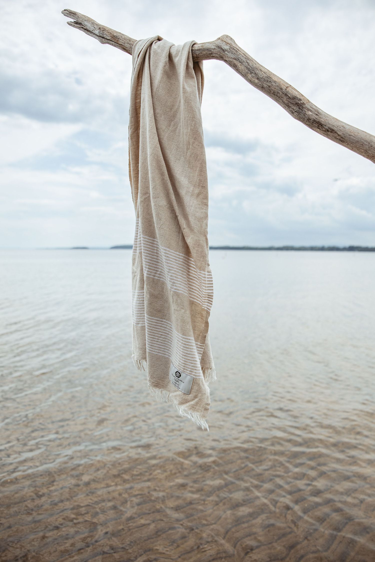 Beige towel hanging from driftwood branch over calm ocean waters.