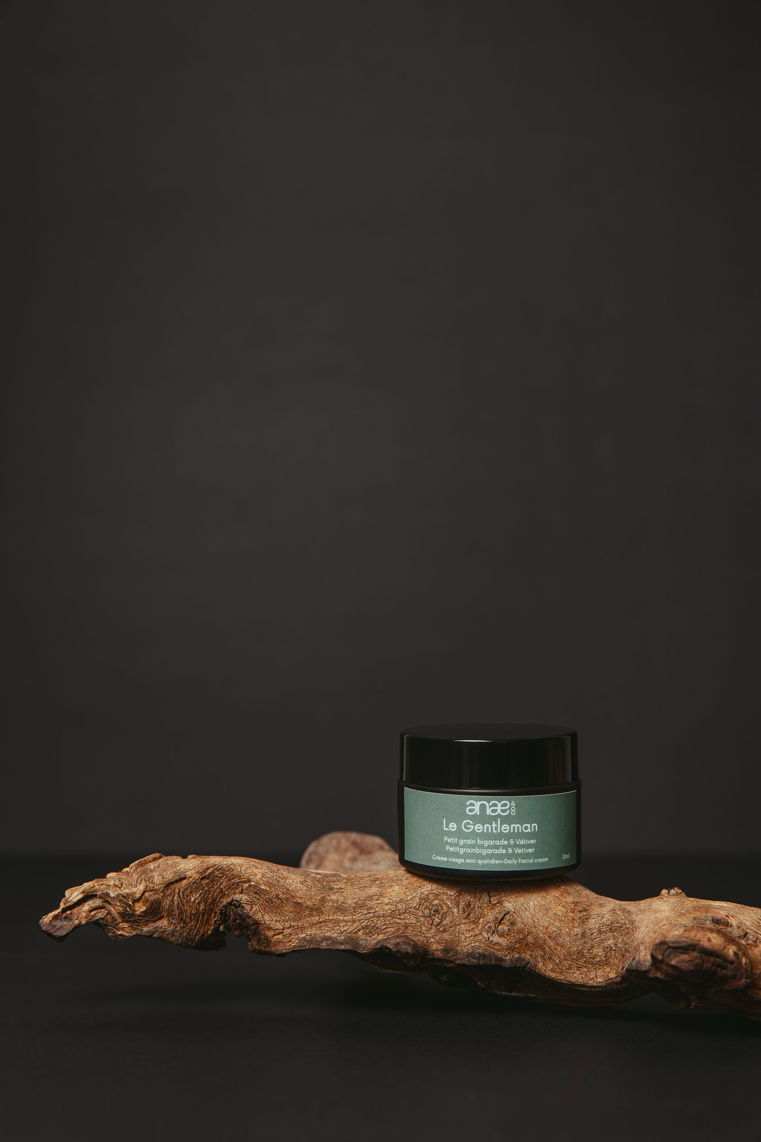 A rustic piece of driftwood displayed alongside dark cosmetic or skincare product containers against a black background.