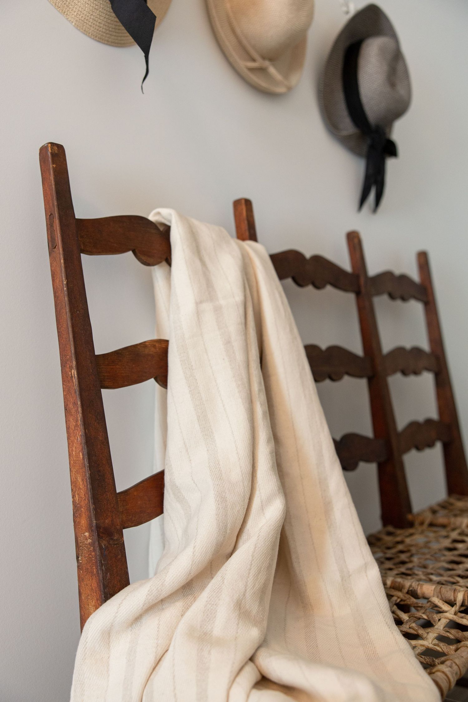 A series of wooden ladder-back chairs with woven seats and white fabric draped over their backs.