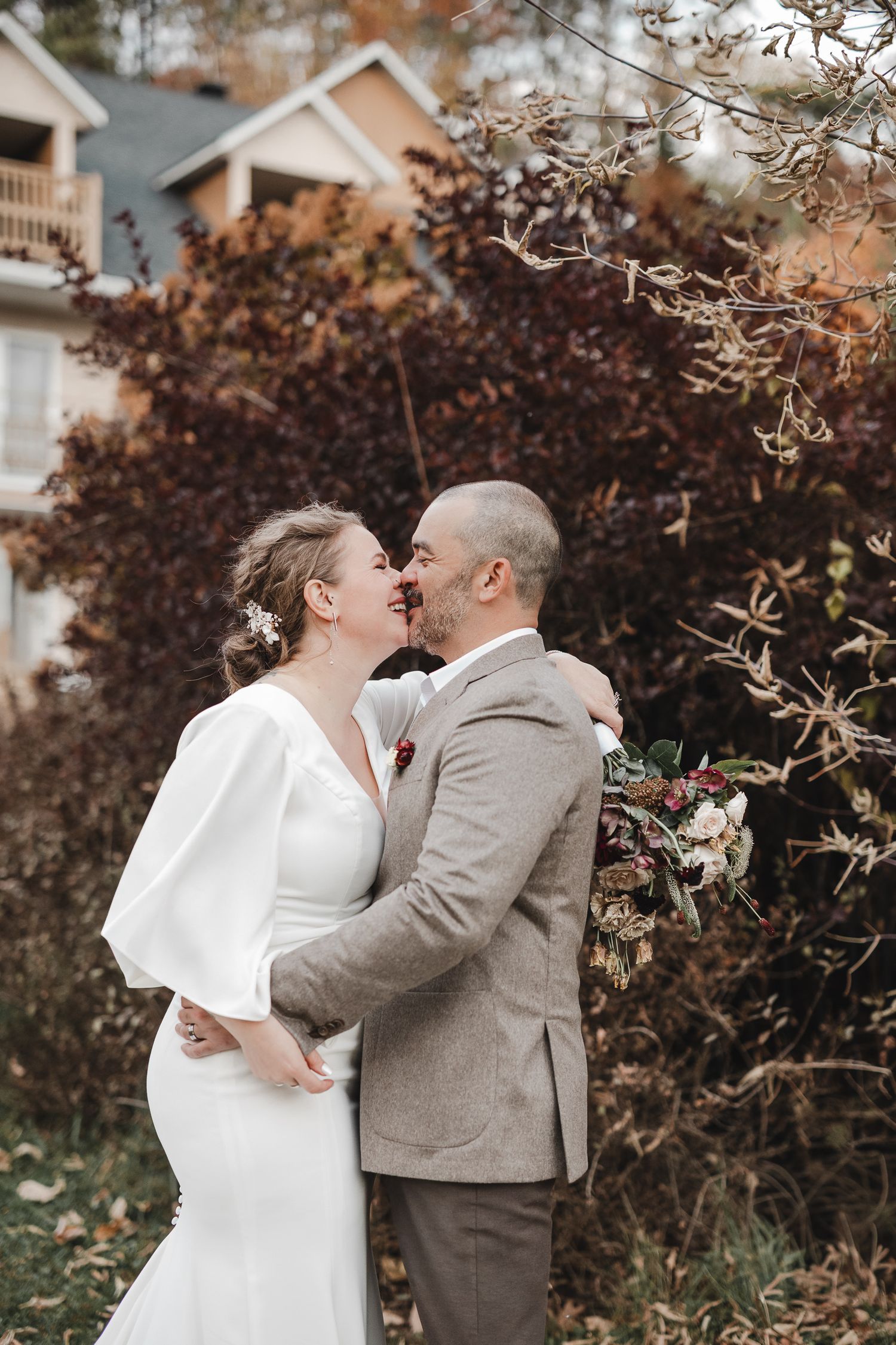 Moment romantique de mariage en extérieur à l’automne, avec feuillage coloré et maisons en arrière-plan.