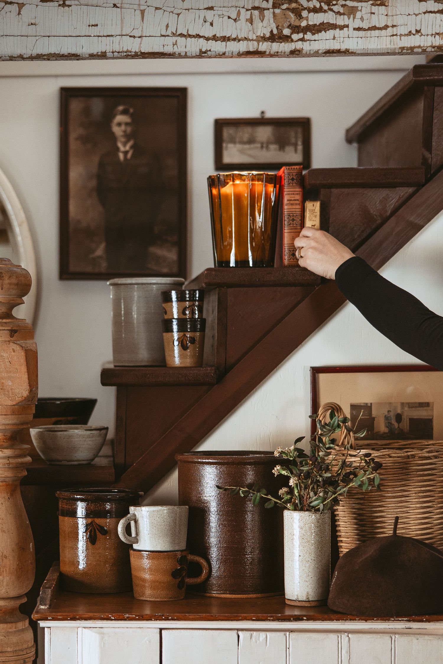 A series of rustic wooden shelves displaying vintage-style pottery, plants and decor items in a cozy interior setting.