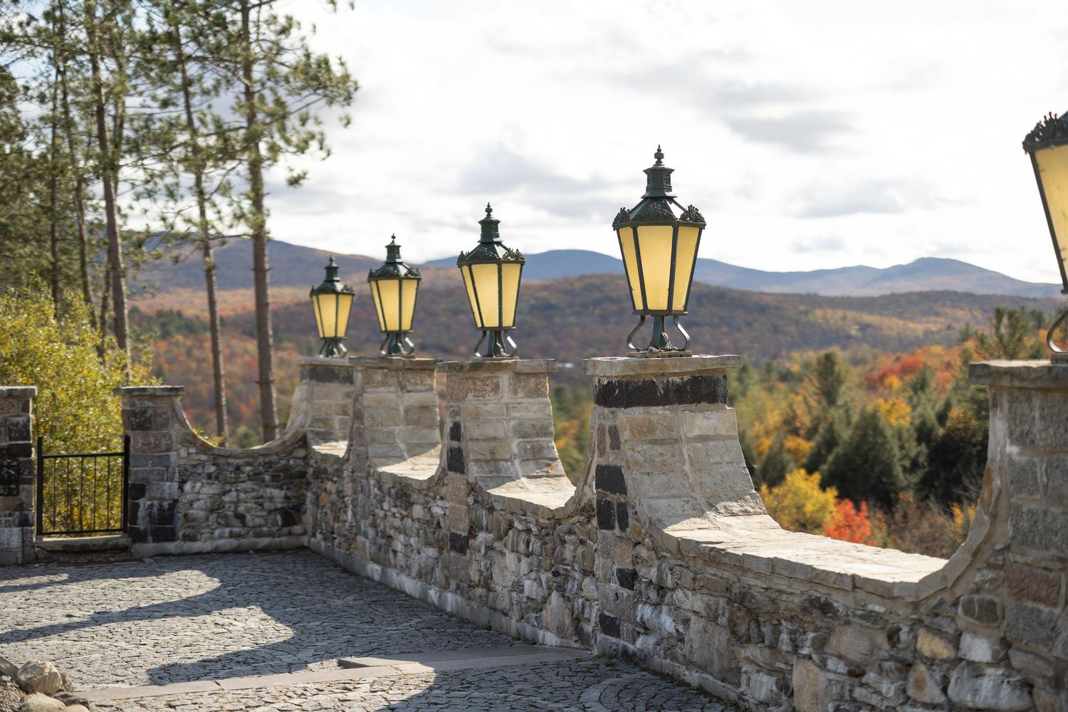 Stone terrace with antique lanterns overlooking a scenic mountain landscape with autumn foliage in the distance.