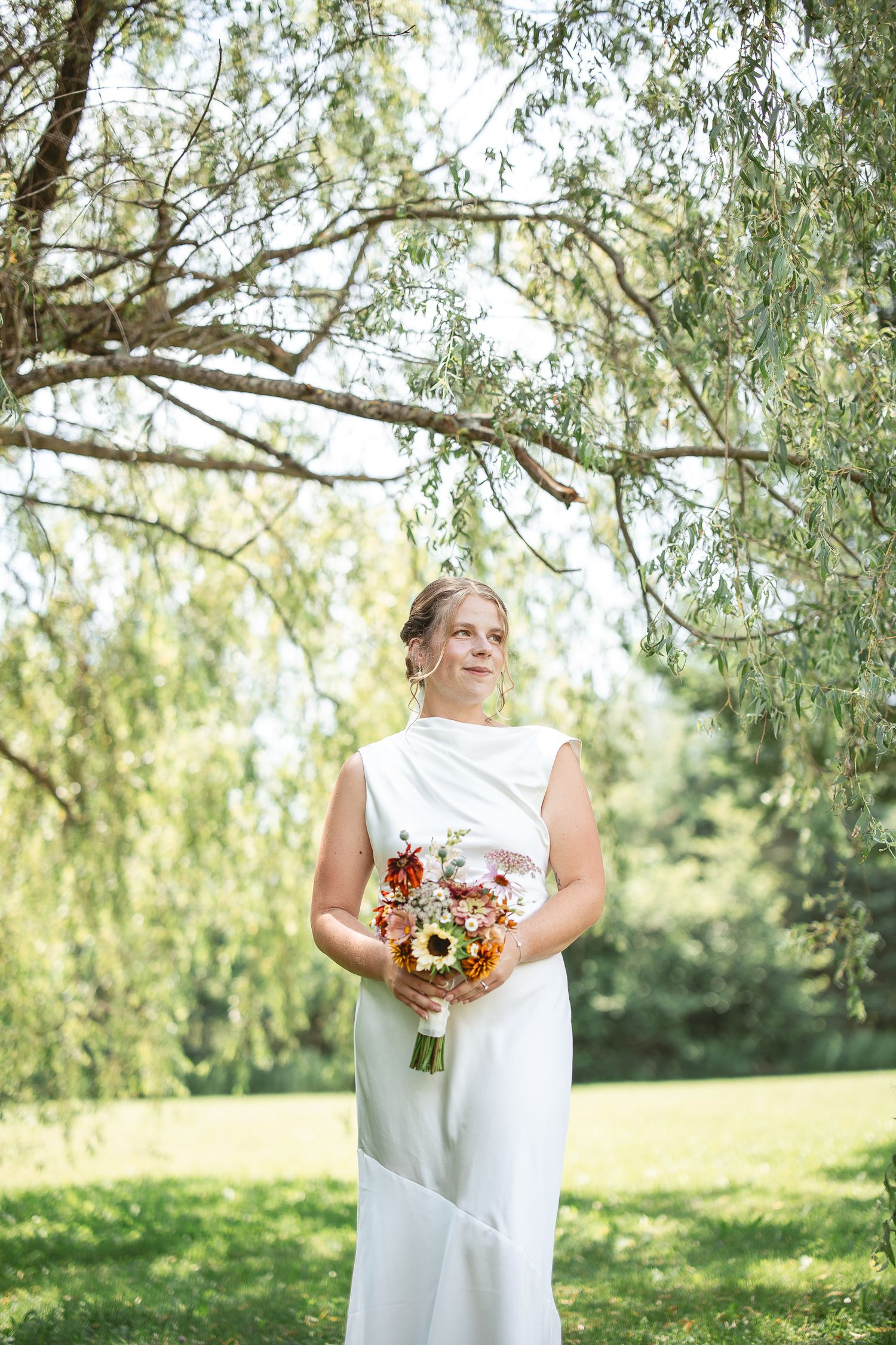 Mariée en robe blanche tenant un bouquet de tournesols sous un saule, par une journée ensoleillée