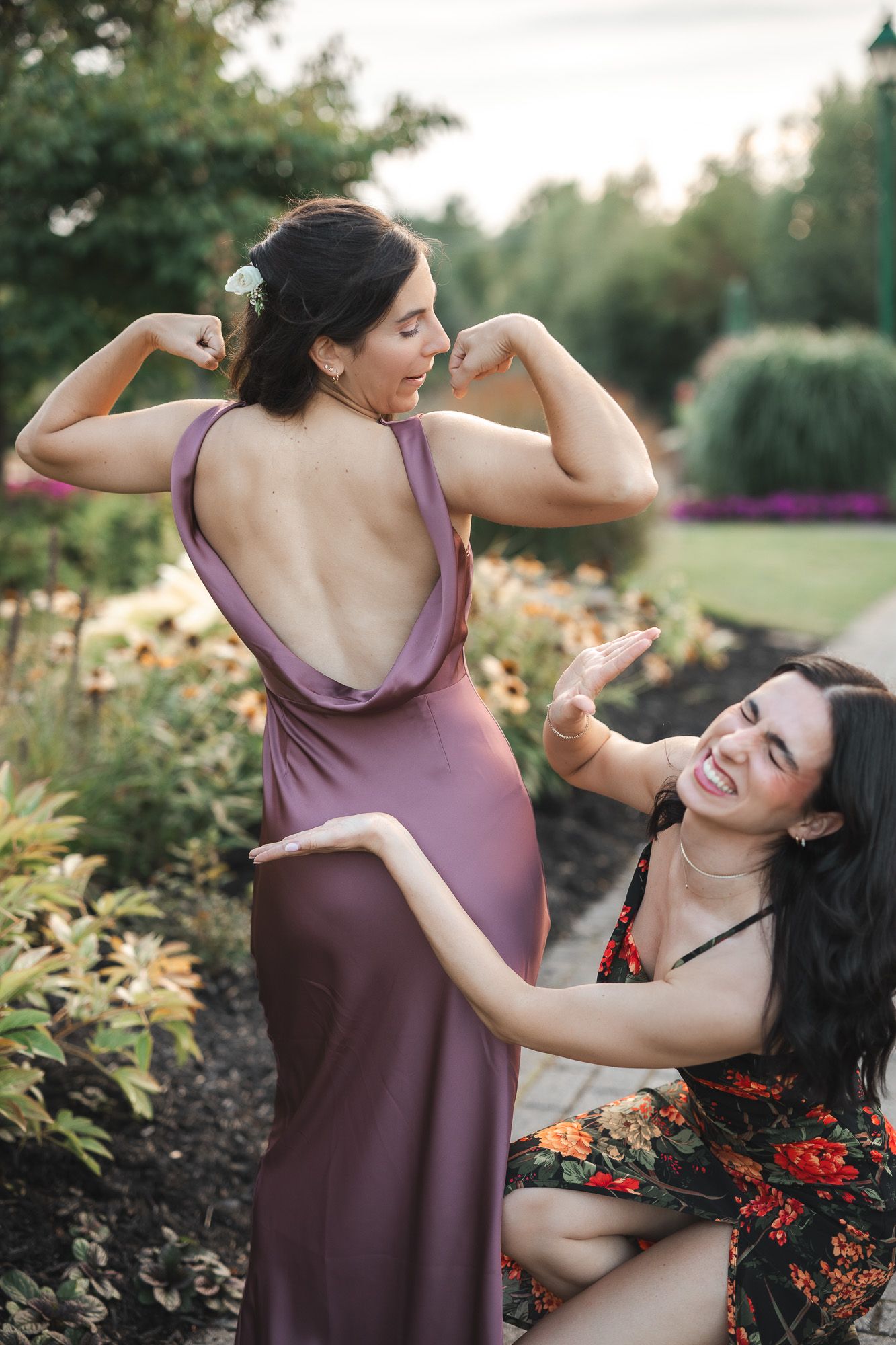 Deux amies riant et posant de façon ludique dans un jardin au coucher du soleil, en robes violette et fleurie