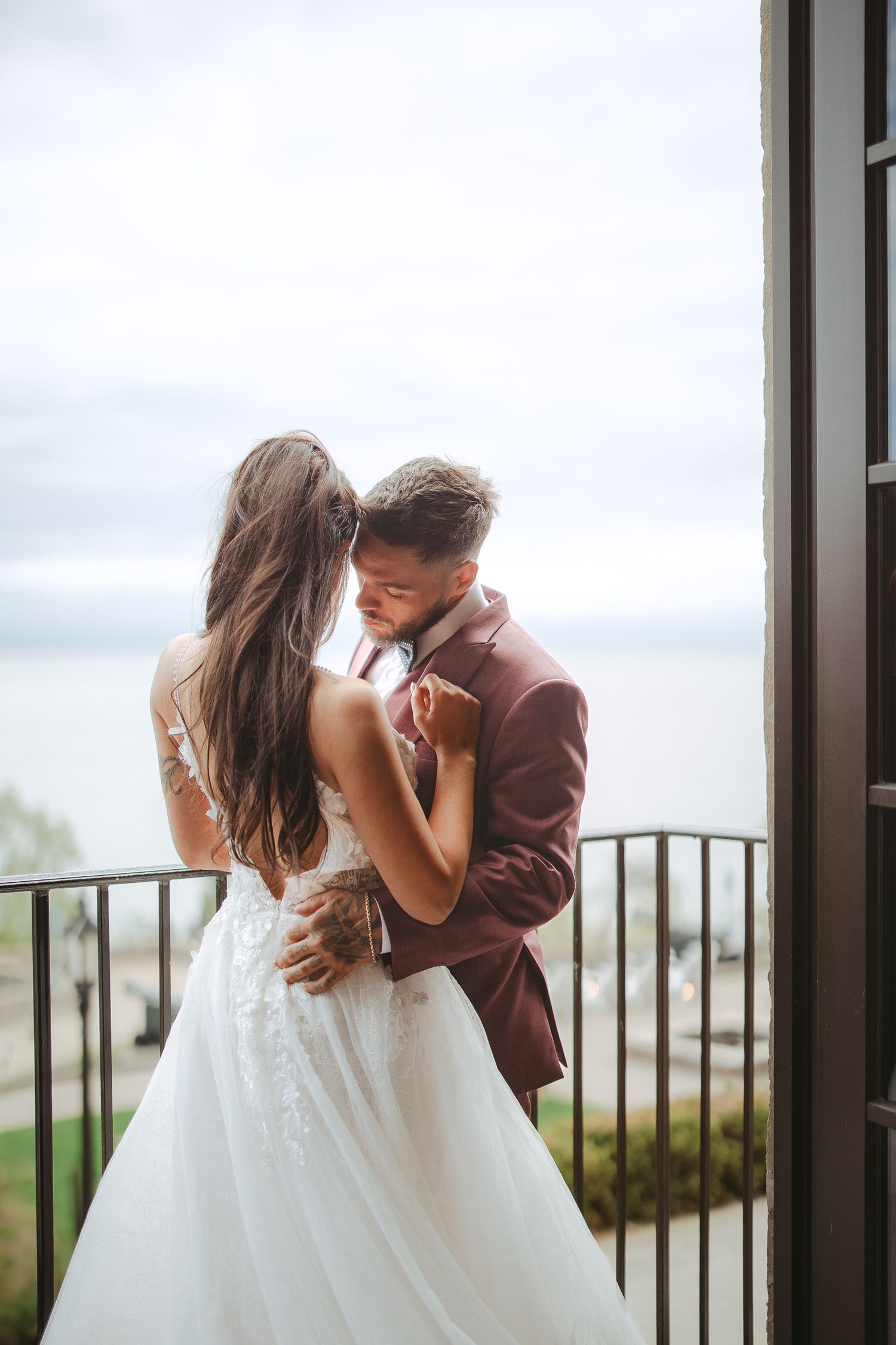 A couple in wedding attire share a romantic kiss on a balcony overlooking a scenic landscape.