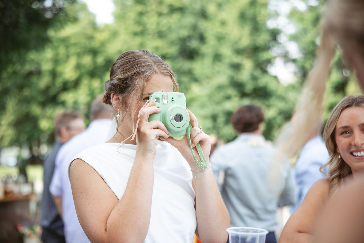 Mariee prenant une photo avec un appareil instantané Fujifilm Instax vert menthe lors d’un événement extérieur