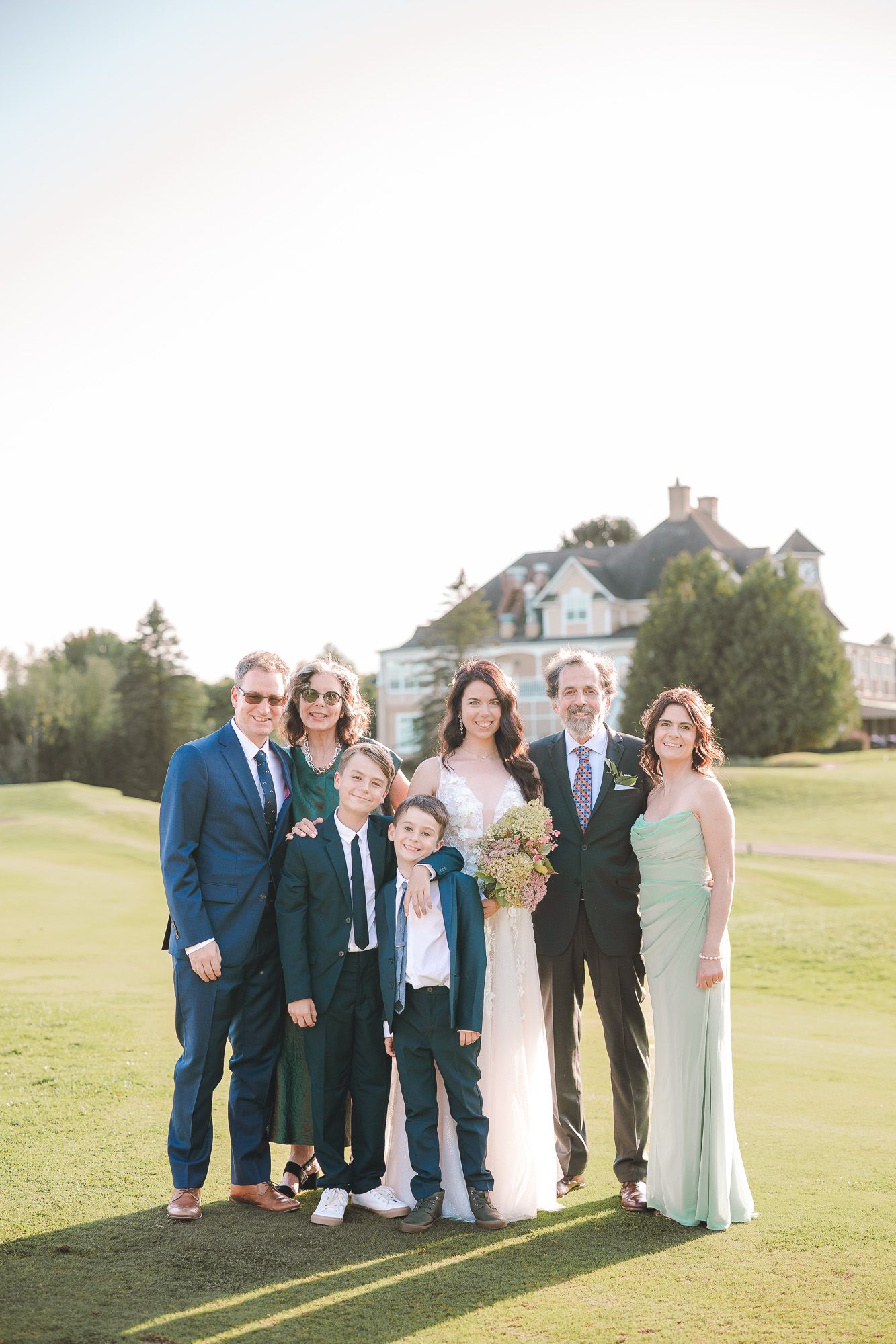 Cortège de mariage posant ensemble sur un terrain de golf ensoleillé, pelouse verdoyante et maisons en arrière-plan, en Estrie