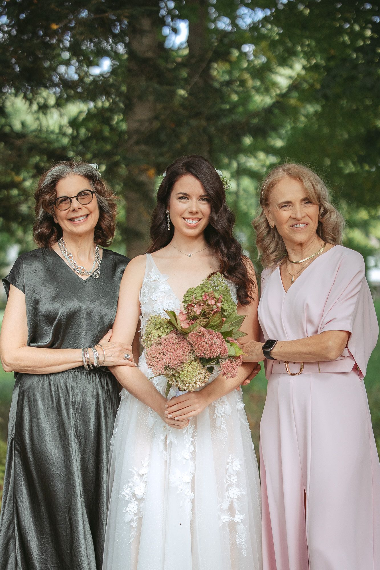 Membres du cortège de mariage en tenues coordonnées grises et roses posant ensemble en extérieur, dans un jardin