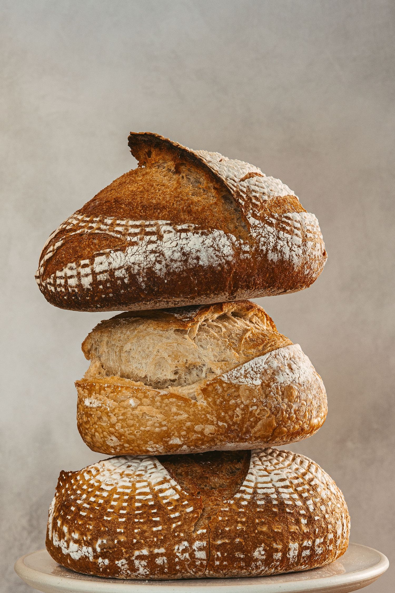 Artisanal sourdough bread loaves stacked on white plates showing crusty textures.