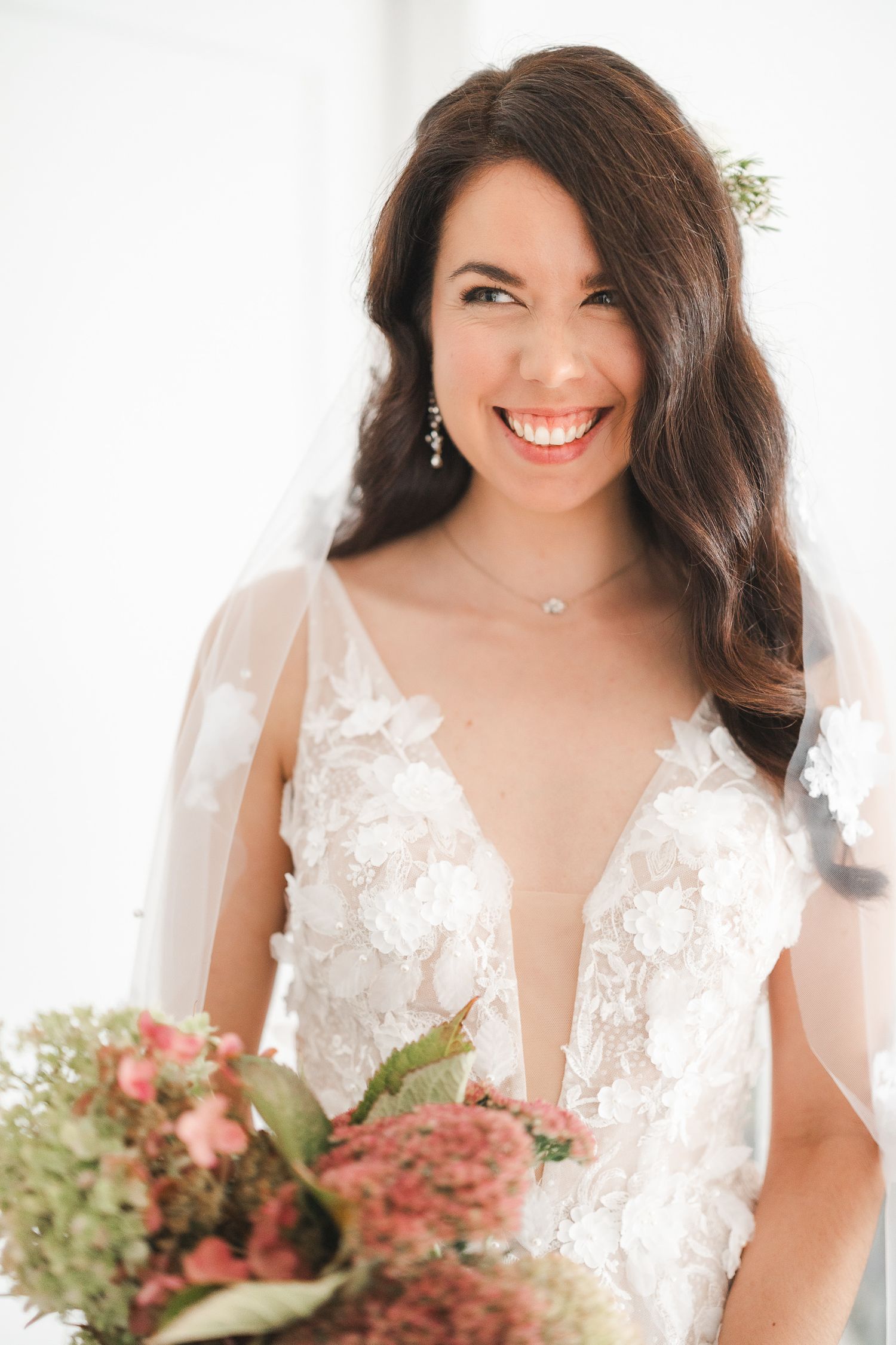 Beautiful bride wearing a plunging v-neck lace wedding gown with delicate floral details and holding a pink bouquet.
