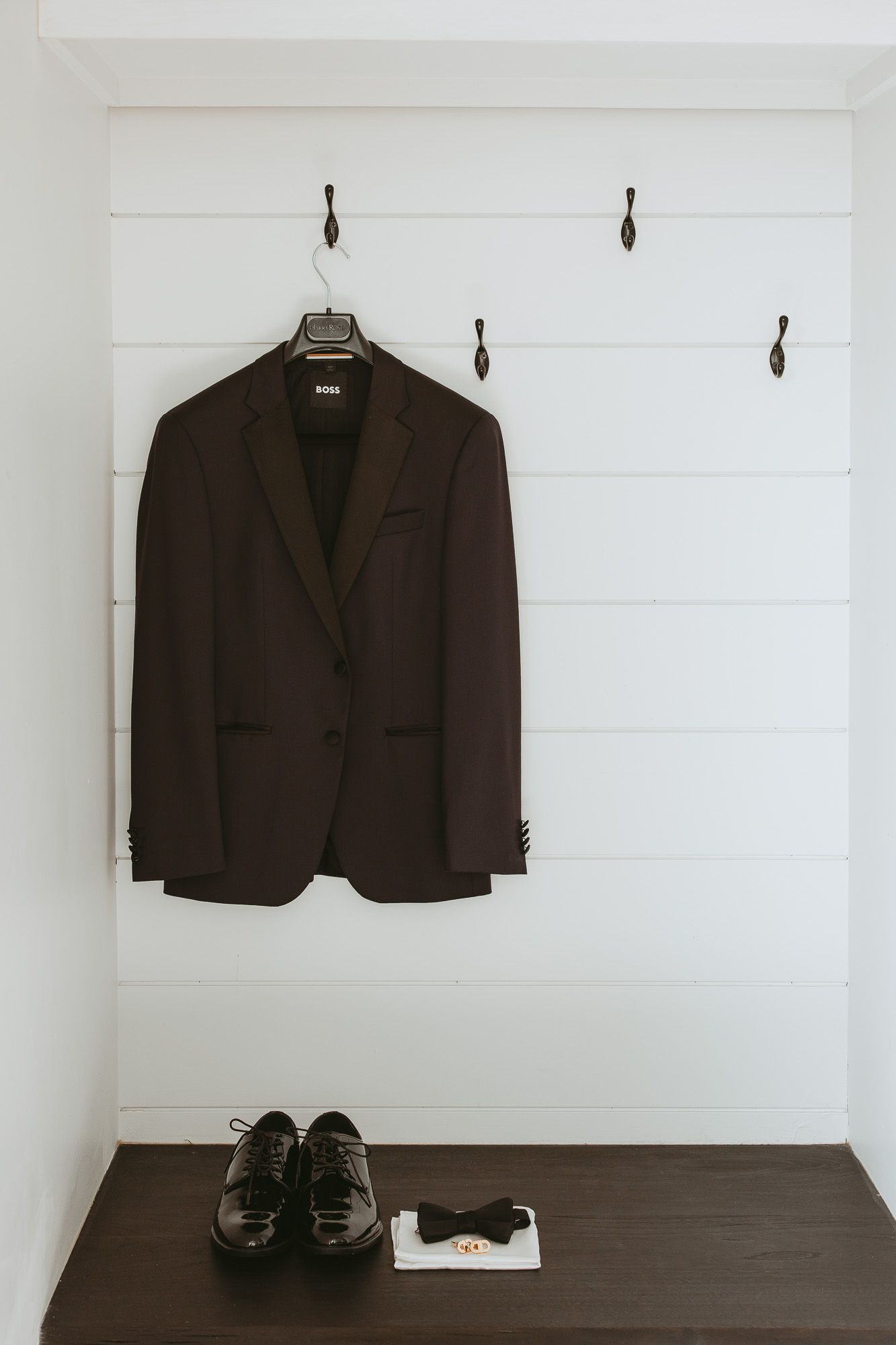 Veste de complet foncée suspendue au mur, avec chaussures habillées et nœud papillon sur surface en bois, mariage en Estrie