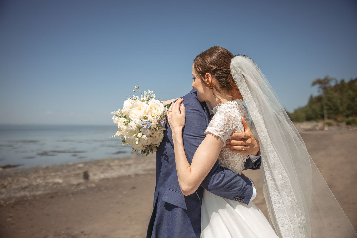 Couple de mariés partageant un moment intime au coucher du soleil, le long d’une plage au décor naturel et romantique.