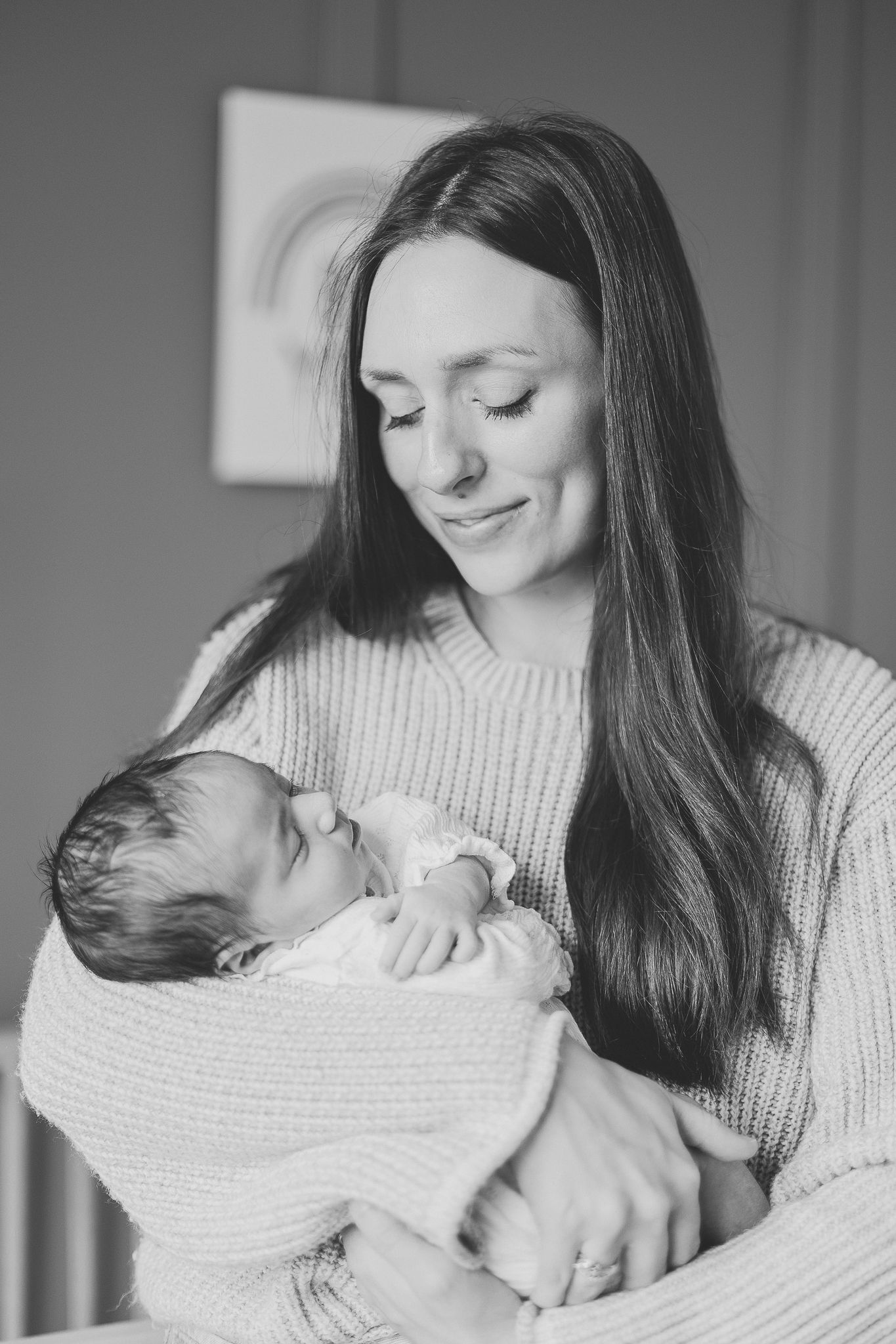 Photographie intime en noir et blanc : parent tenant son bébé en pull confortable à domicile, pour valoriser douceur et complicité