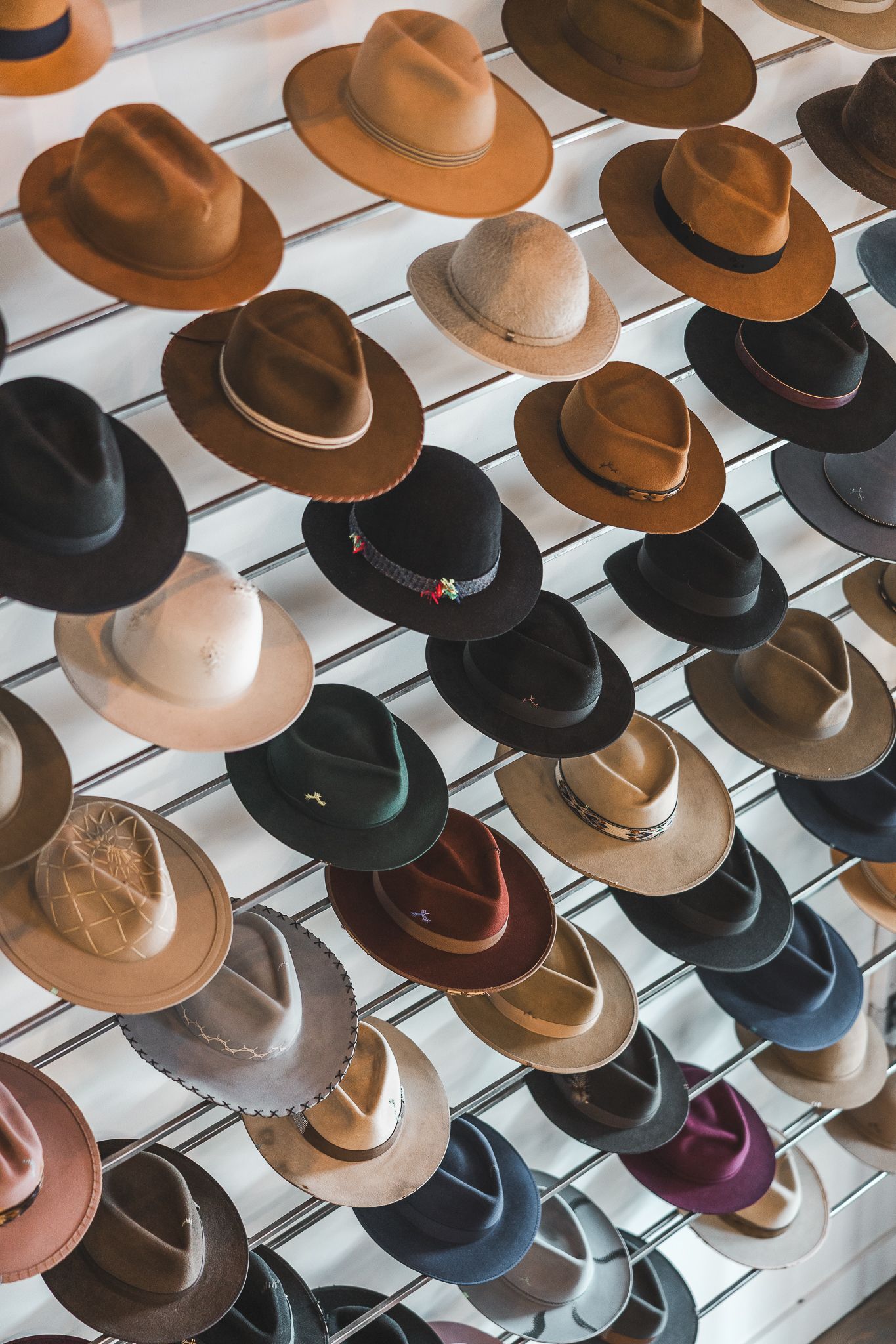 Une collection de chapeaux de cowboy de style western, bruns et noirs, est exposée sur des supports muraux blancs dans un magasin.