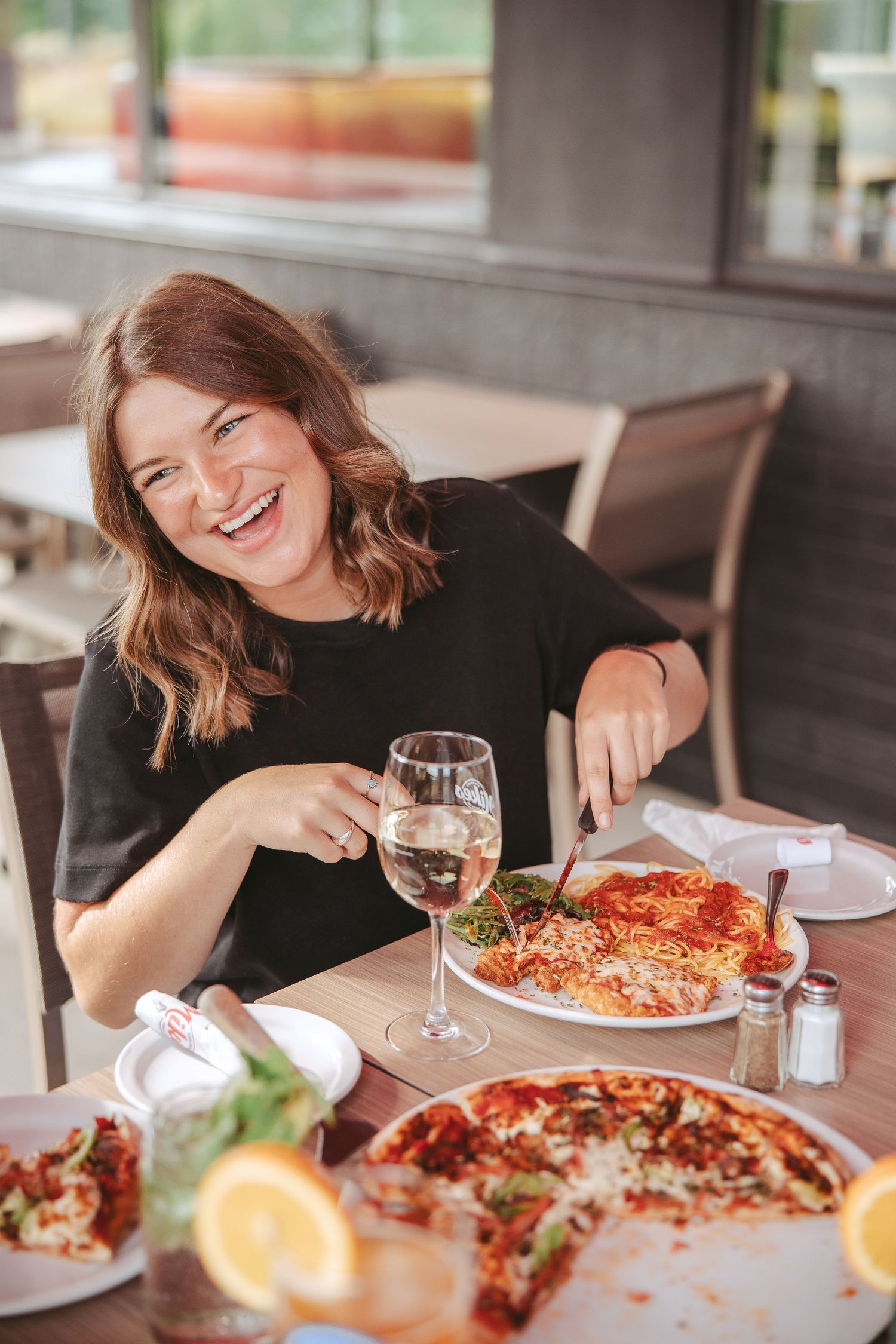 A casual dining scene with wine glasses and Italian dishes on a wooden table at an outdoor restaurant.