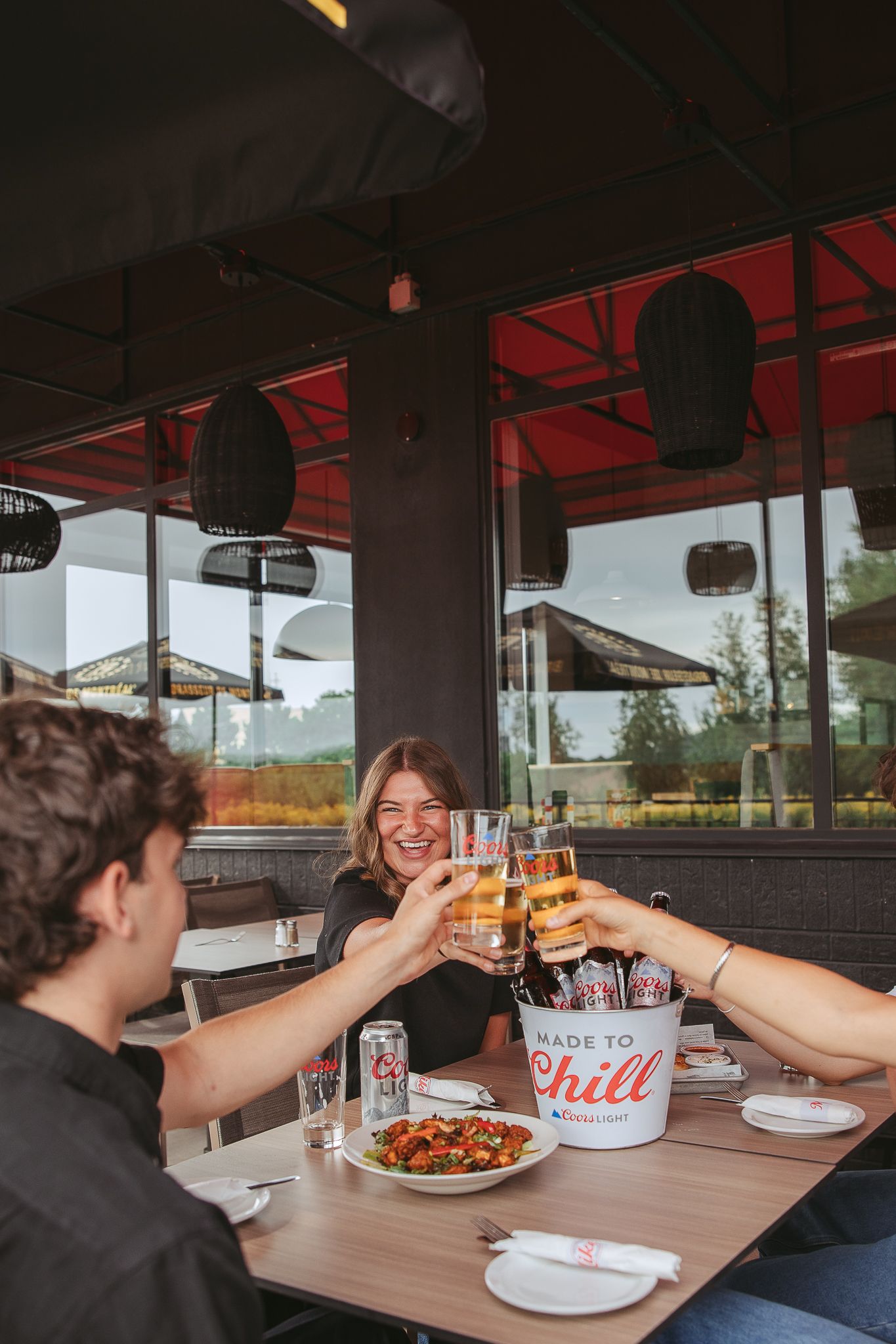 Friends toasting with wine glasses and sharing a meal at a restaurant booth with red decor.