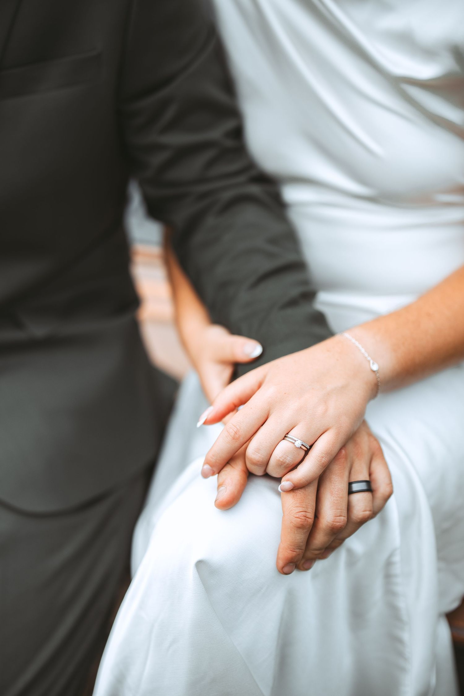 Close-up series of hands wearing wedding rings against white dress and dark suit fabric backgrounds.
