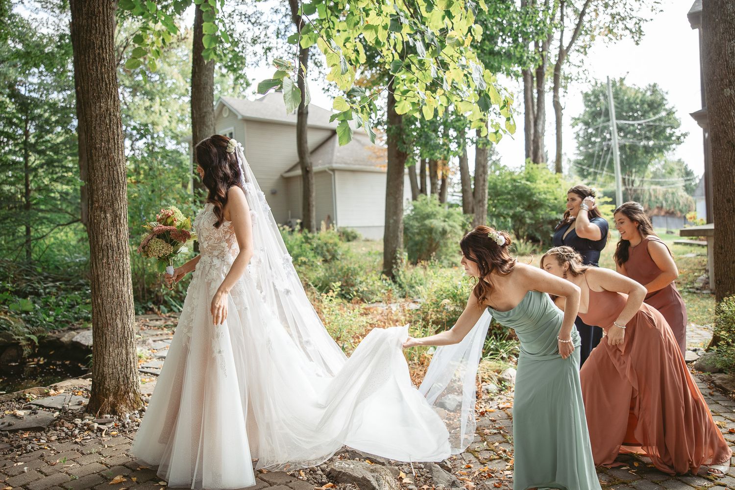 Membres du cortège de mariage réunis en extérieur sous les arbres, en robes vert sauge et tons rouille