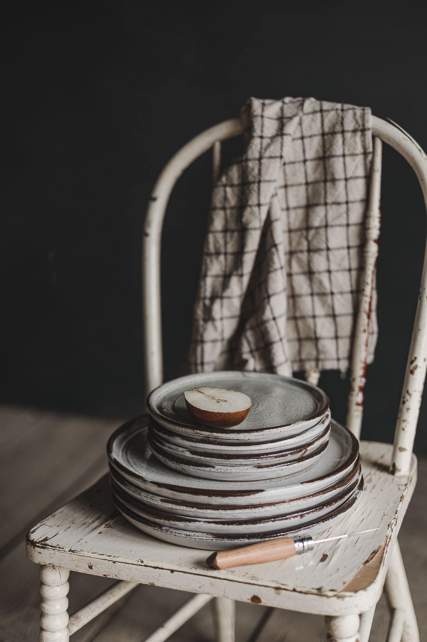 Série d’images montrant des assiettes en poterie empilées sur une chaise blanche vieillie, captées pour valoriser le produit et ses détails
