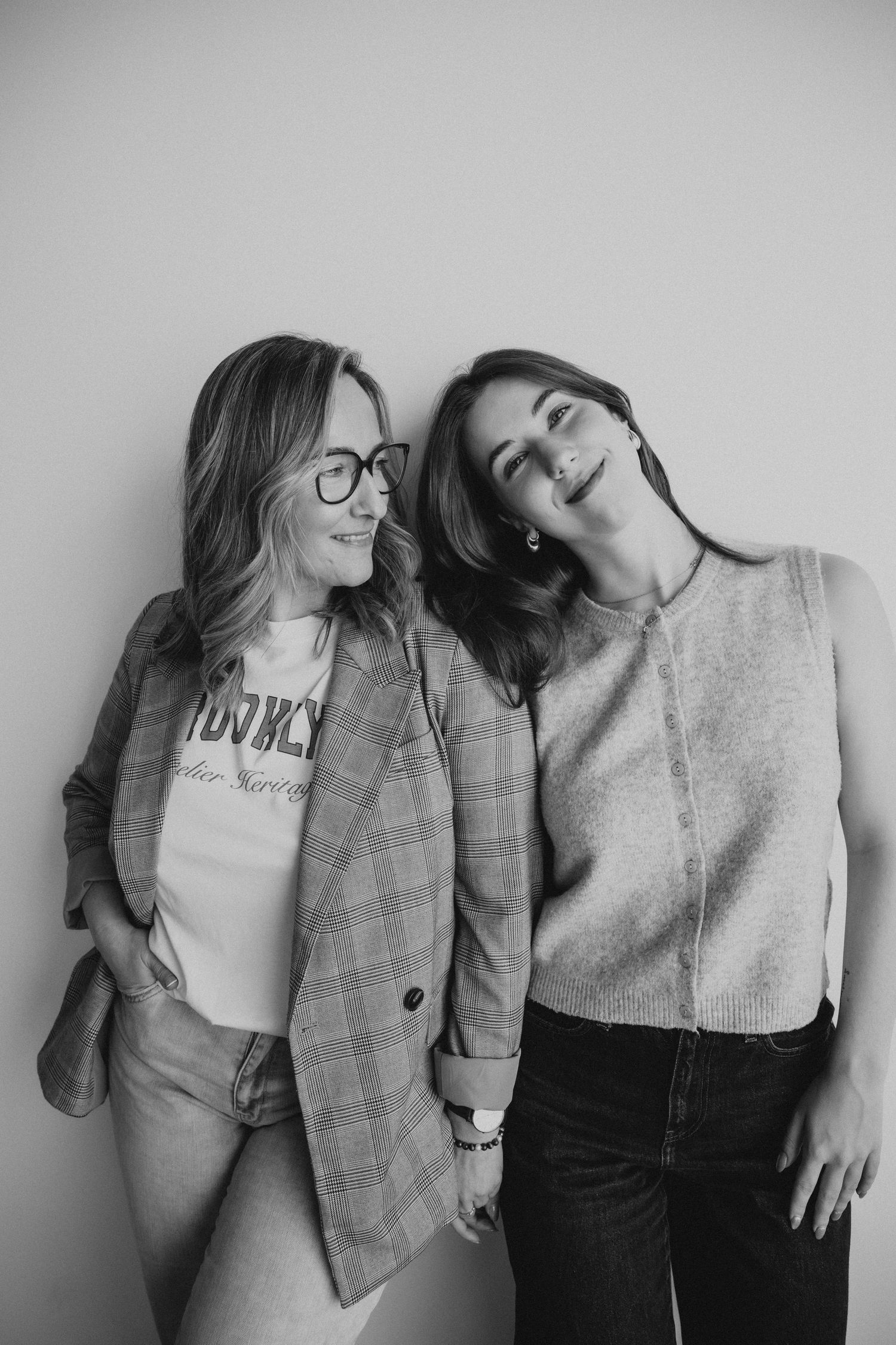 Two friends in casual attire pose together against a gray wall in a series of candid black and white photographs.