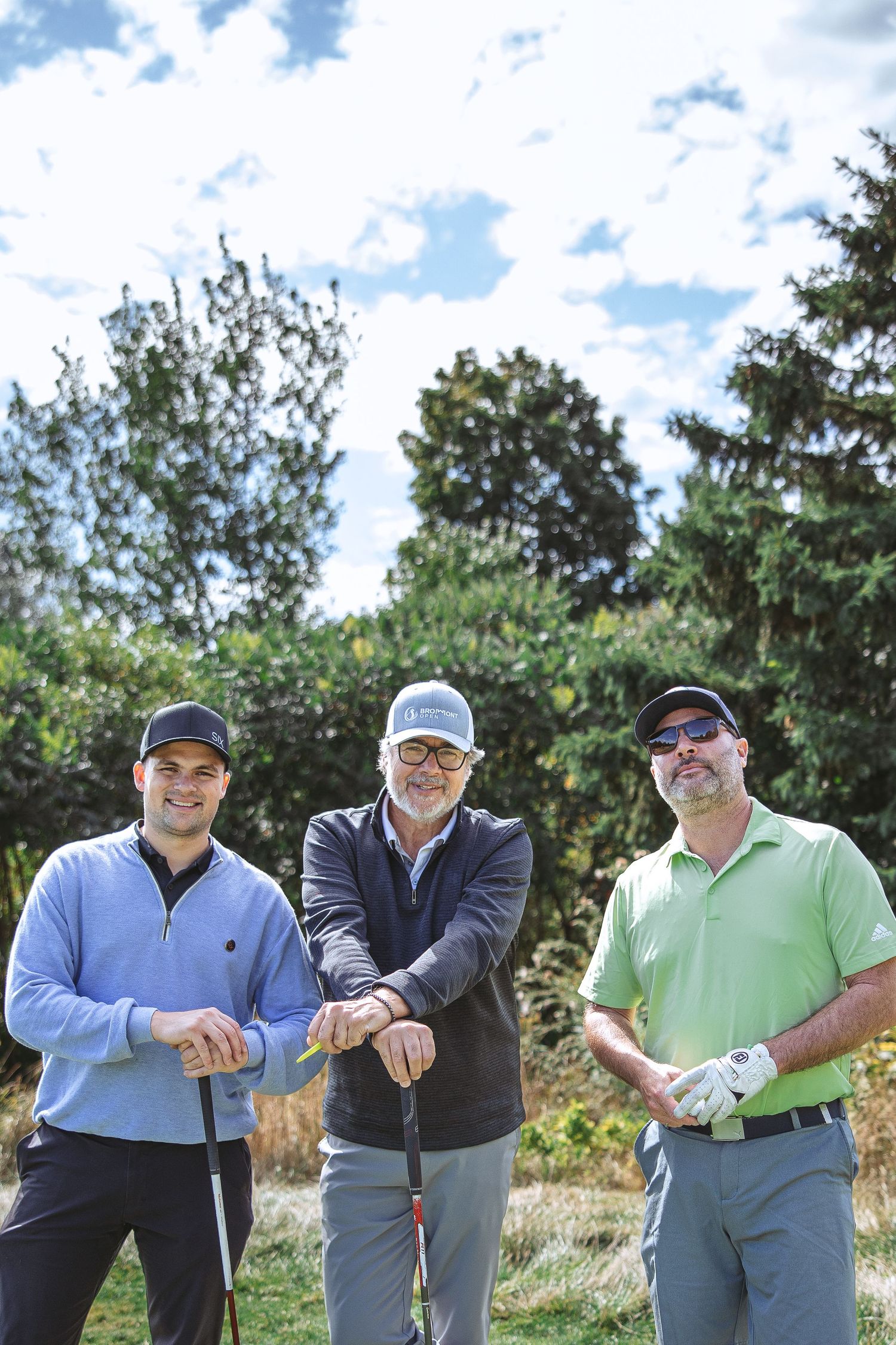 A group of golfers posing together on a sunny day at a golf course with trees in the background.
