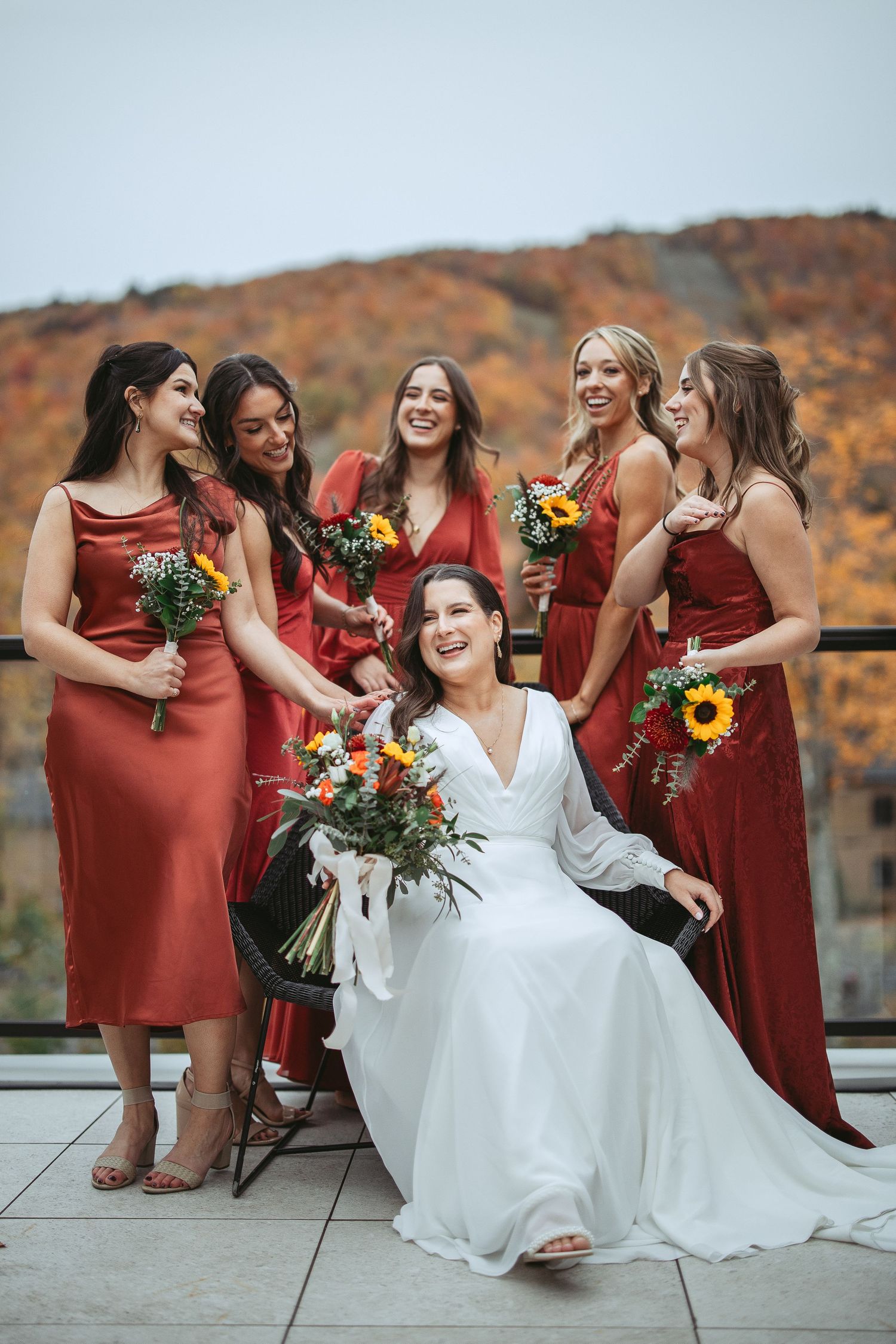 Wedding party wearing burgundy bridesmaid dresses and white gown pose together against autumn mountain backdrop.