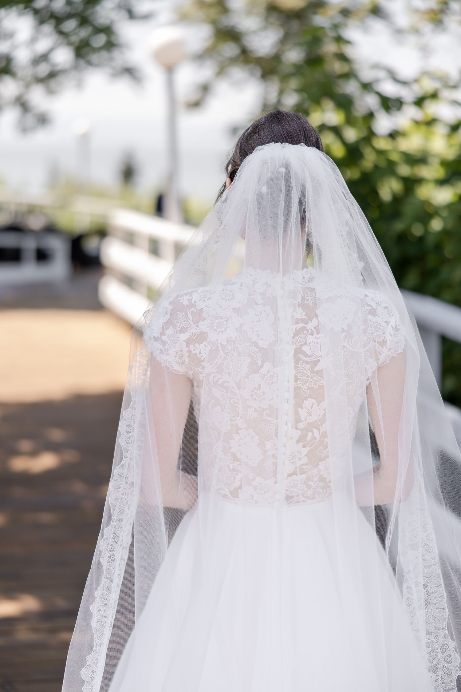 A delicate white lace wedding veil with intricate embroidery details blowing gently in the breeze outdoors.