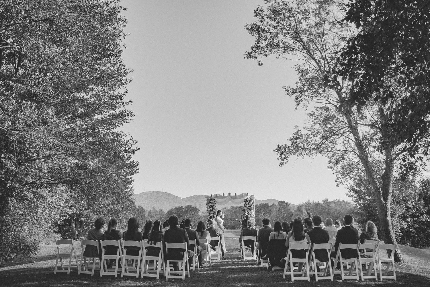 Cérémonie de mariage en plein air en noir et blanc, invités assis en rangées face à un décor montagneux