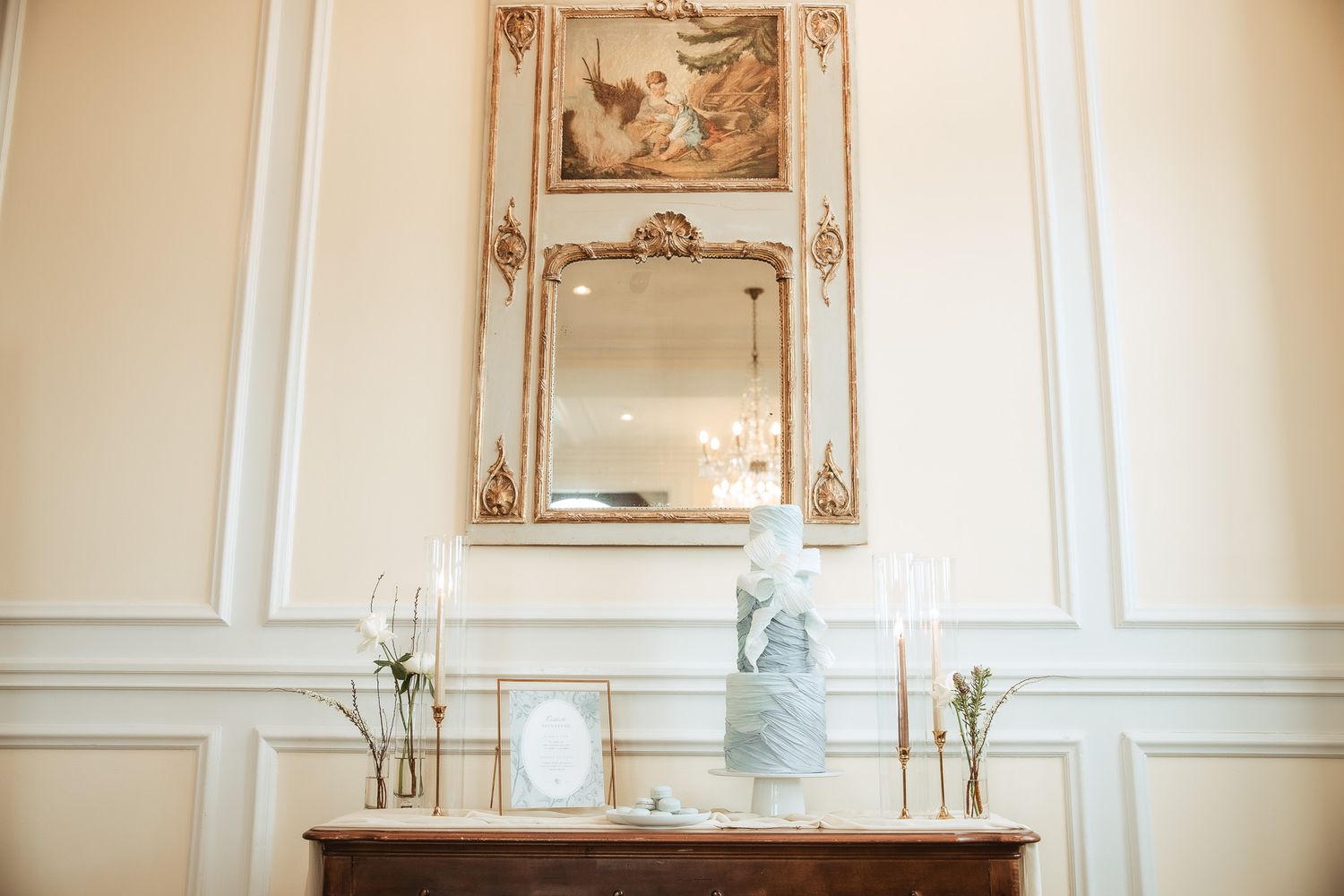 Pièce élégante aux murs crème avec moulures décoratives et œuvres encadrées d’or, ambiance classique avec un gâteau de mariage sur un meuble