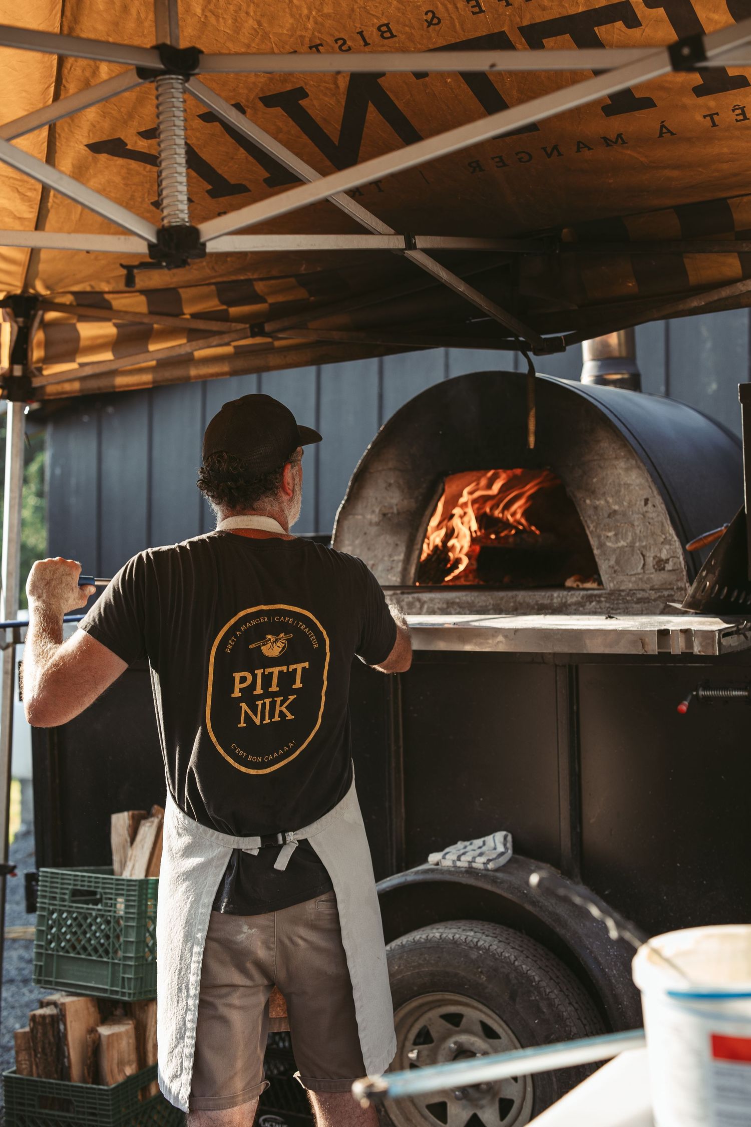 Wood-fired pizza ovens with flames visible in a rustic outdoor kitchen setting.