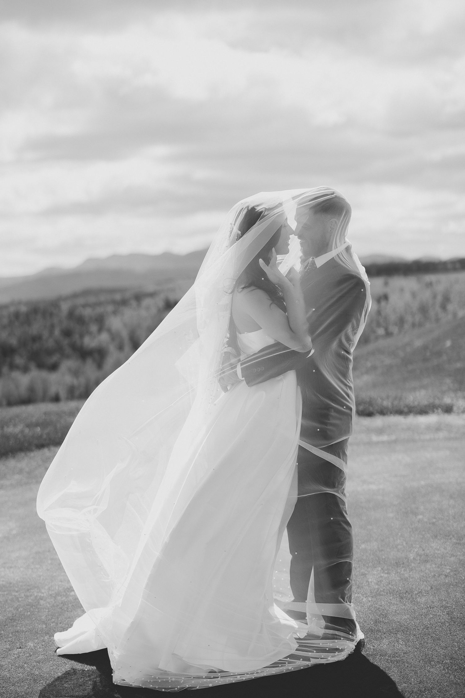 Noir et blanc. Robe de mariée blanche et fluide se déploie de façon spectaculaire dans le vent, au cœur d’un paysage montagneux saisissant.
