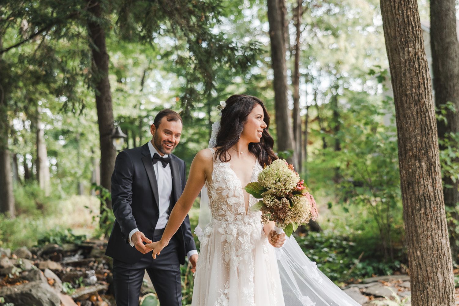 Couple en tenue de mariage marchant dans un décor forestier boisé, cérémonie en Estrie