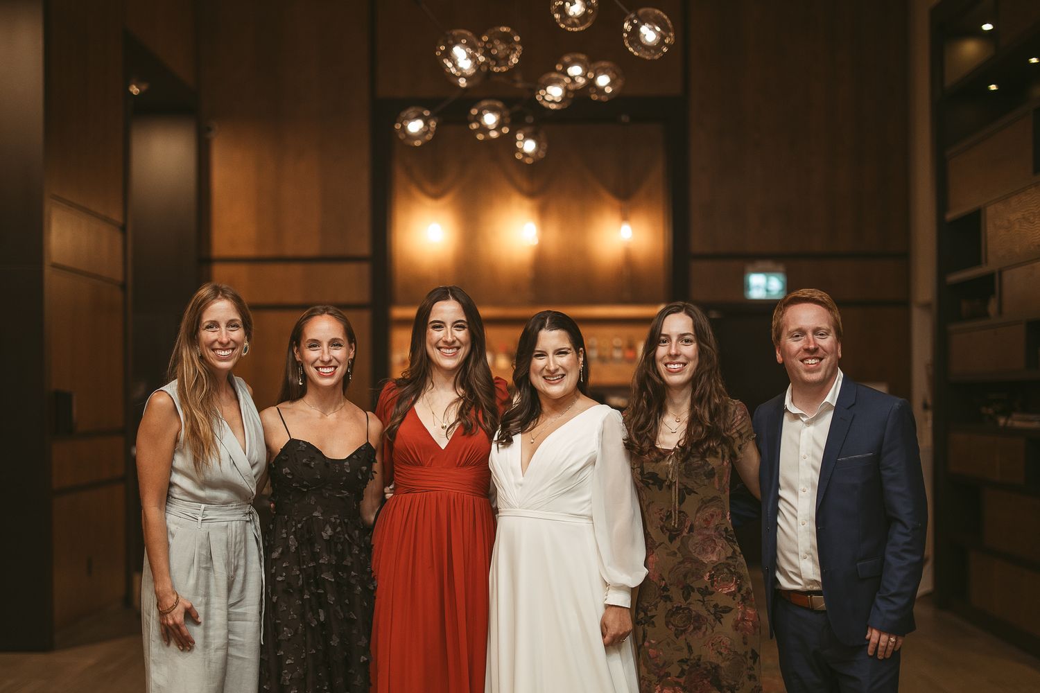 Un groupe d’invités de mariage pose ensemble pour des photos lors d’une réception intérieure, dans une ambiance à l’éclairage chaleureux.